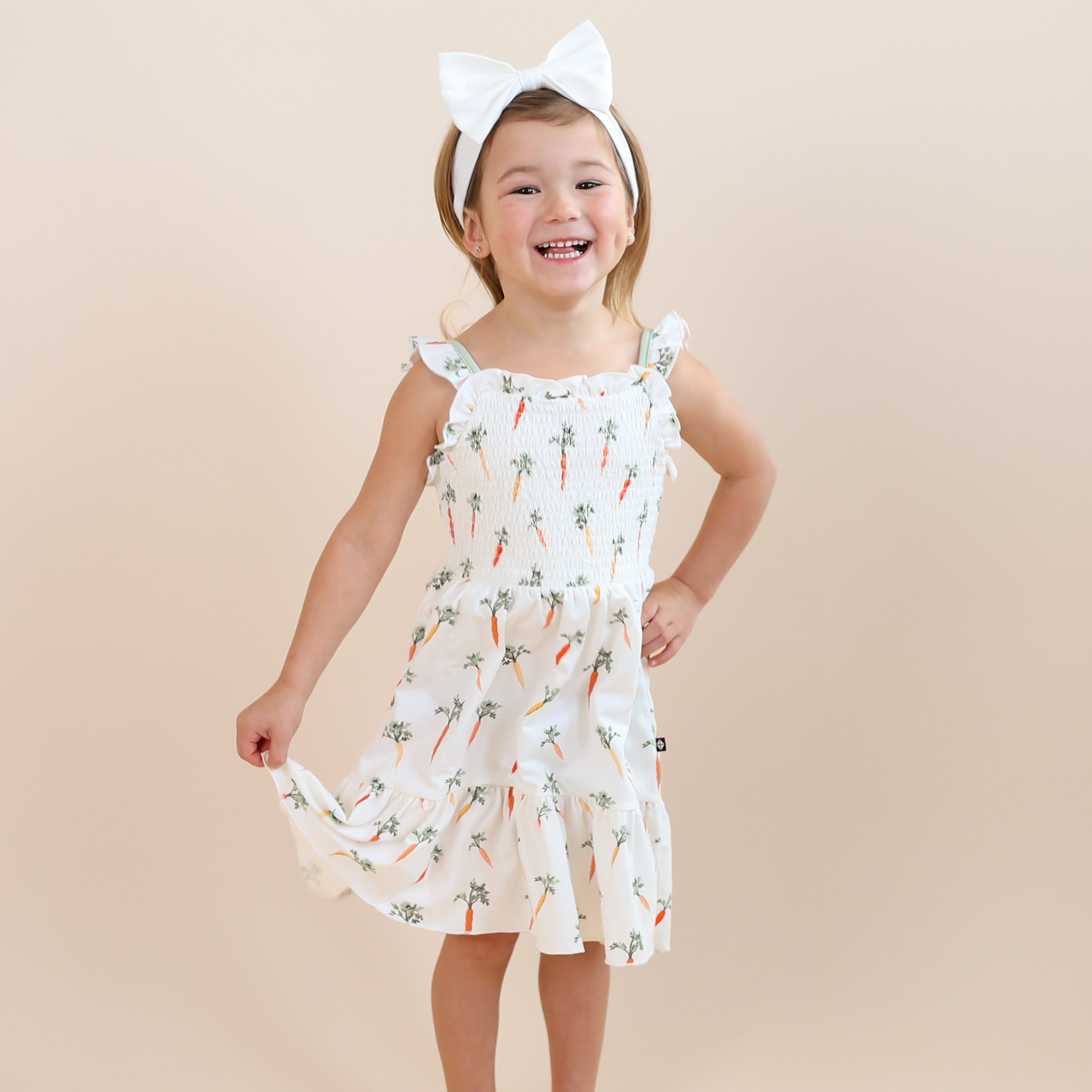 Young girl wearing the Smocked Dress in Carrot paired with a white bow