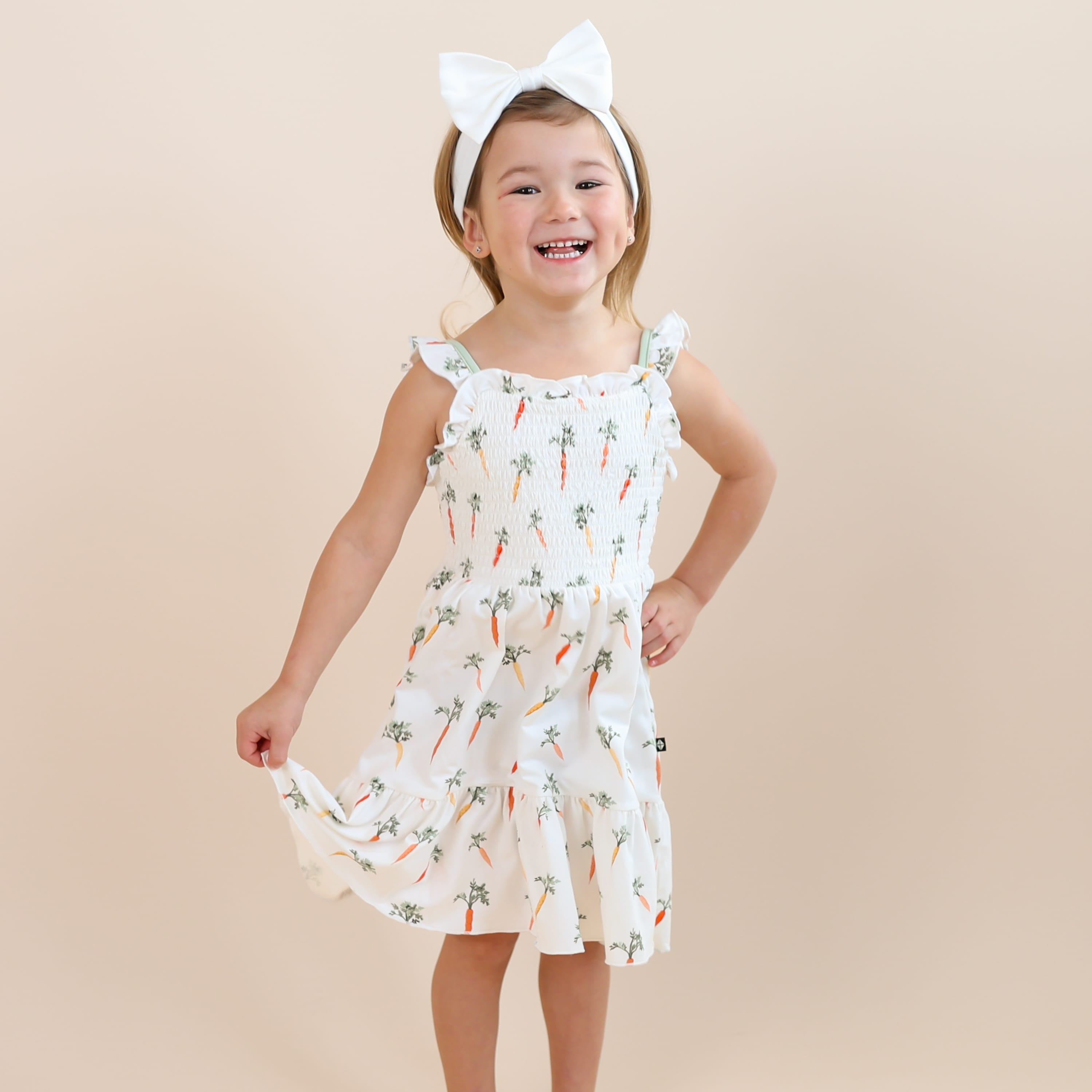 Young girl wearing the Smocked Dress in Carrot paired with a white bow