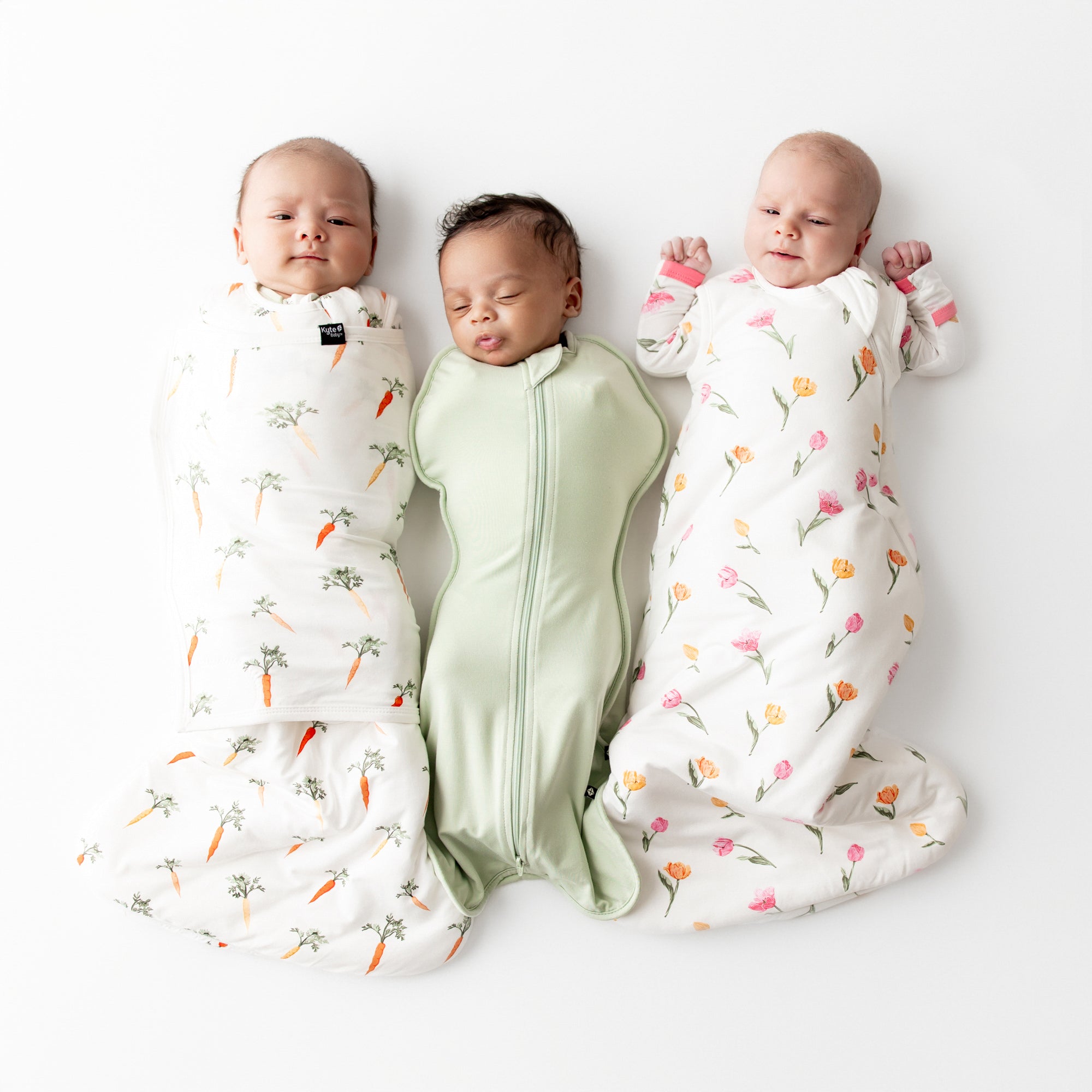 Three newborns laying side by side wearing the Sleep Bag Swaddler in Carrot 1.0 Basil Sleep bag 0.5 and 1.0 sleep bag in tulip