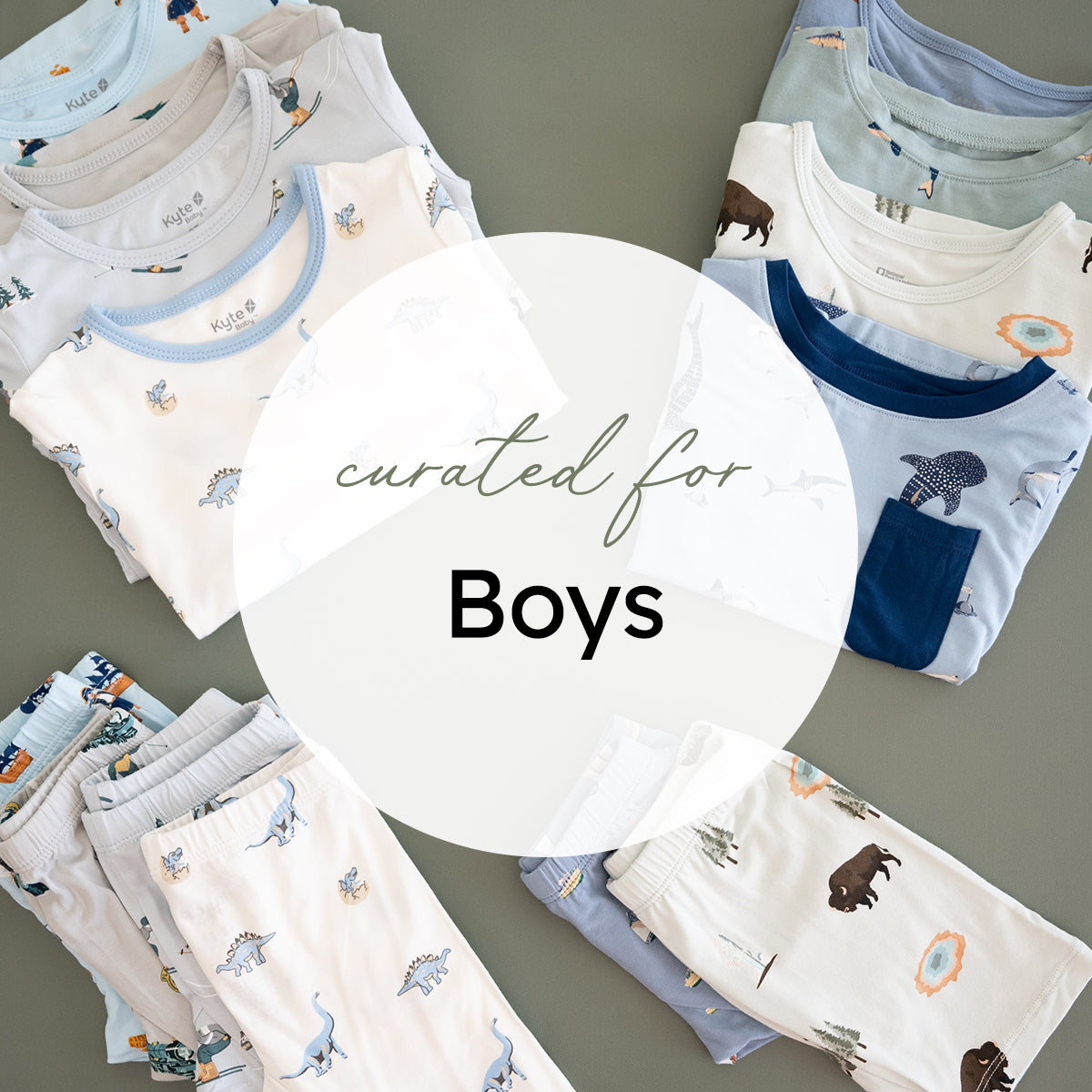 A styled flat-lay of folded children's pajamas and tops arranged around a large white circular overlay that reads 'curated for Boys'. The garments are mostly white and light blue with dinosaur, elephant, and animal prints, photographed on a muted gray-green background.