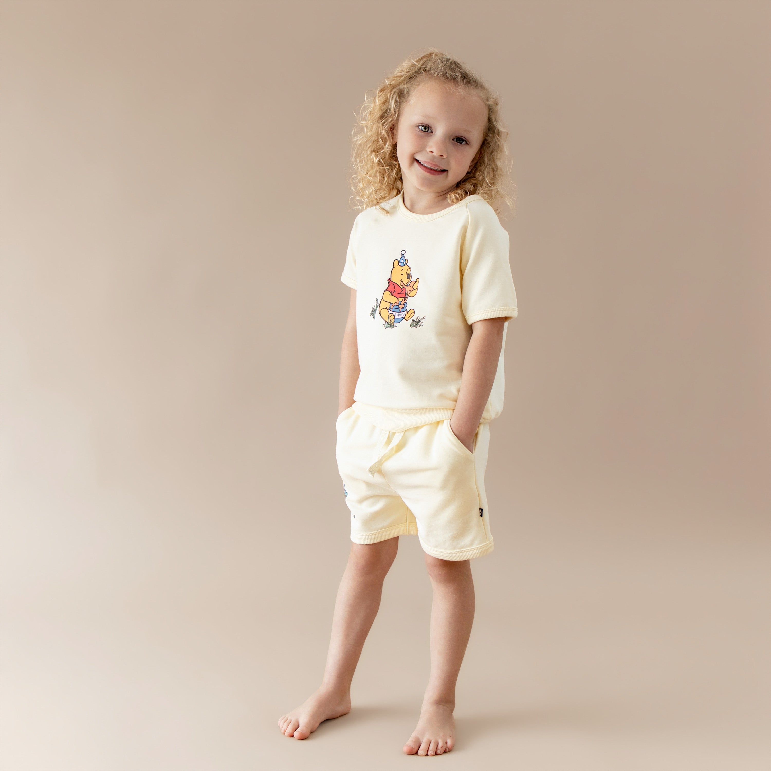 Young girl modeling the Short Sleeve Jogger Set in Winnie the Pooh on Chamomile with her hands in the pocket of the shorts