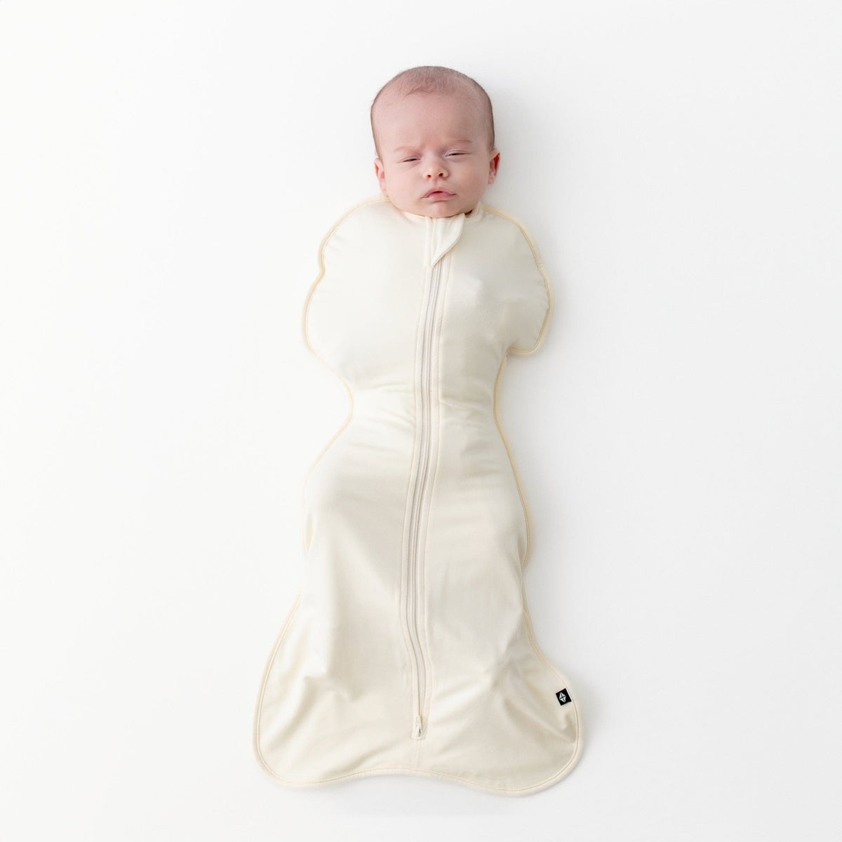 Newborn laying on a light neutral surface wearing the Swaddle Bag in Chamomile 0.5
