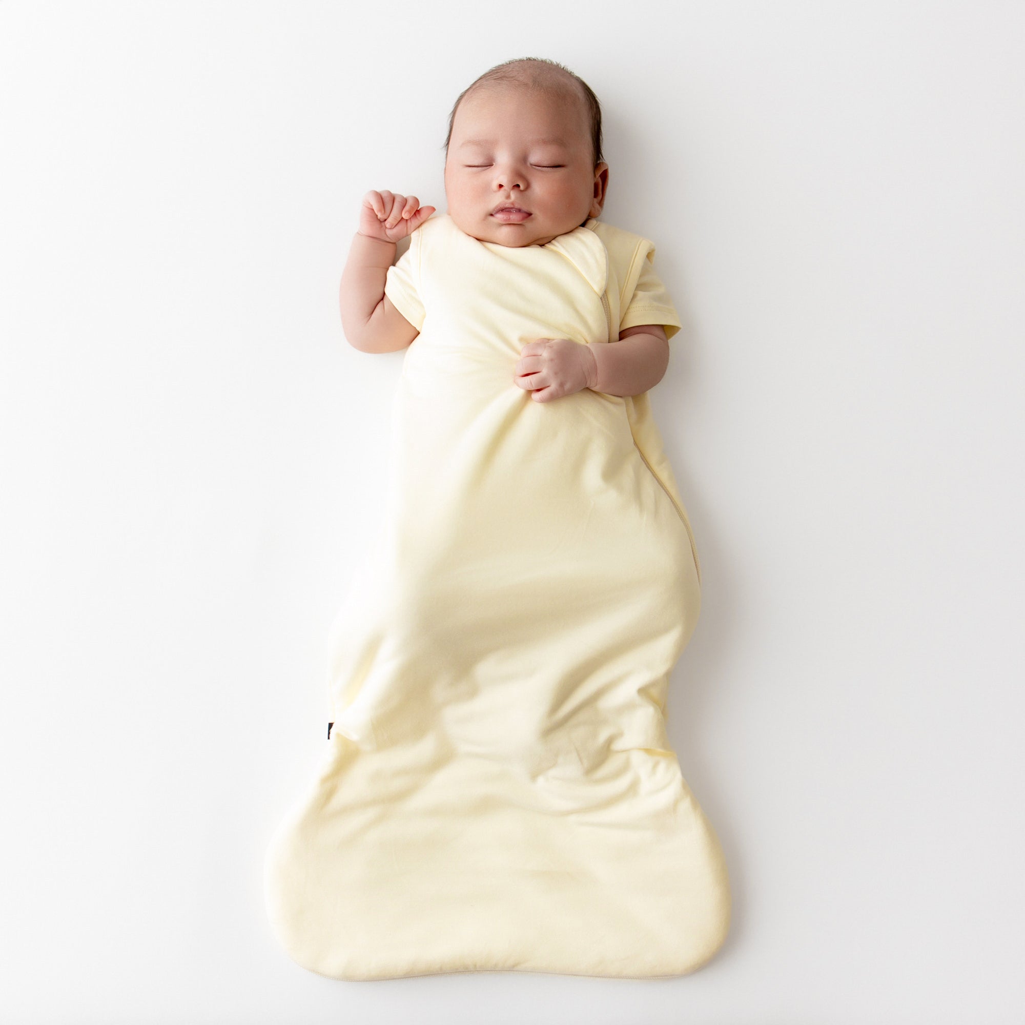Baby asleep wearing a kyte baby sleep bag in a pale yellow color