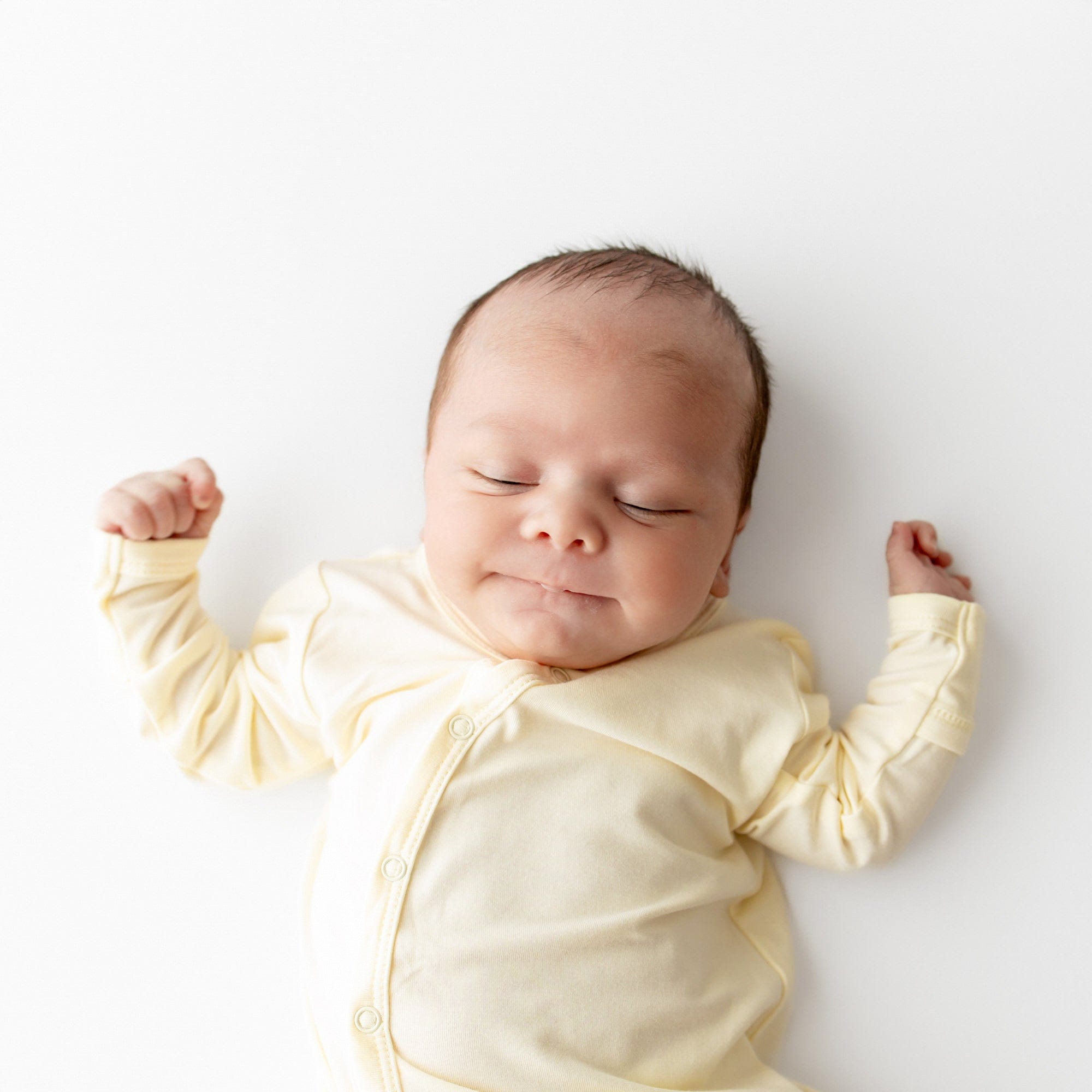 Newborn baby in a yellow outfit lying on a white background