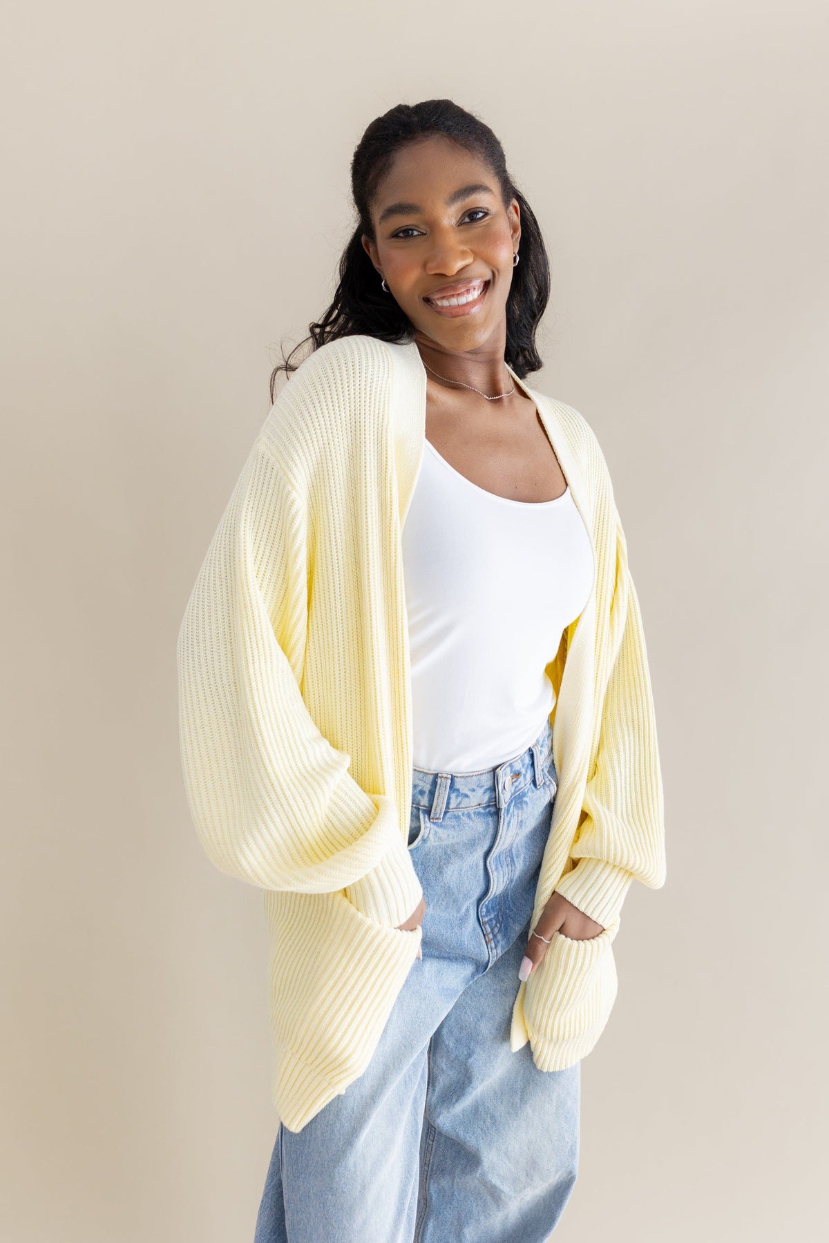 Female model posing wearing the Chunky Knit Women's Oversized Cardigan in Chamomile overtop a white tank top and light wash jeans