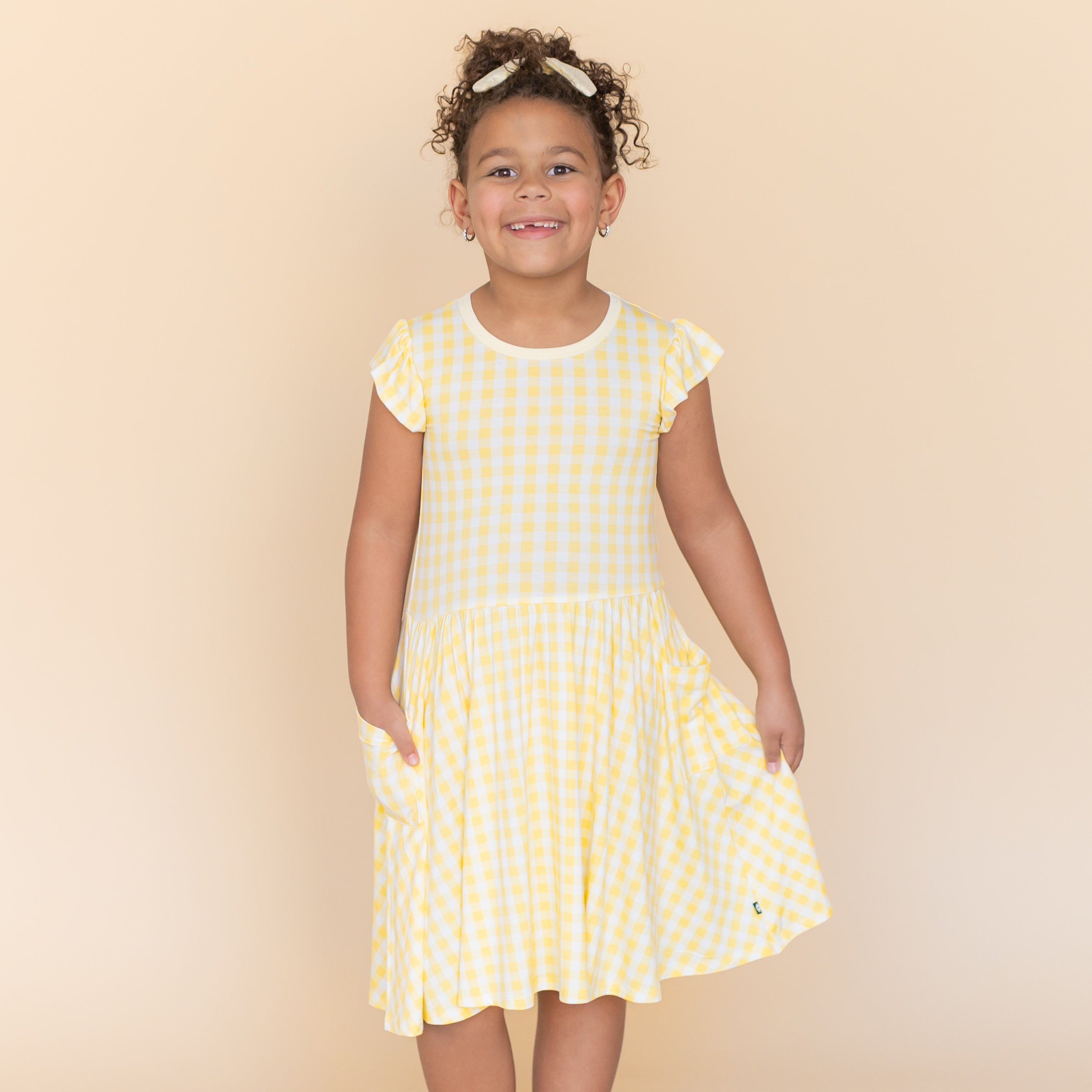 Young girl modeling the Pocket Dress in Gingham Chamomile with one hand in the pocket with the other hand holding the skirt of the dress