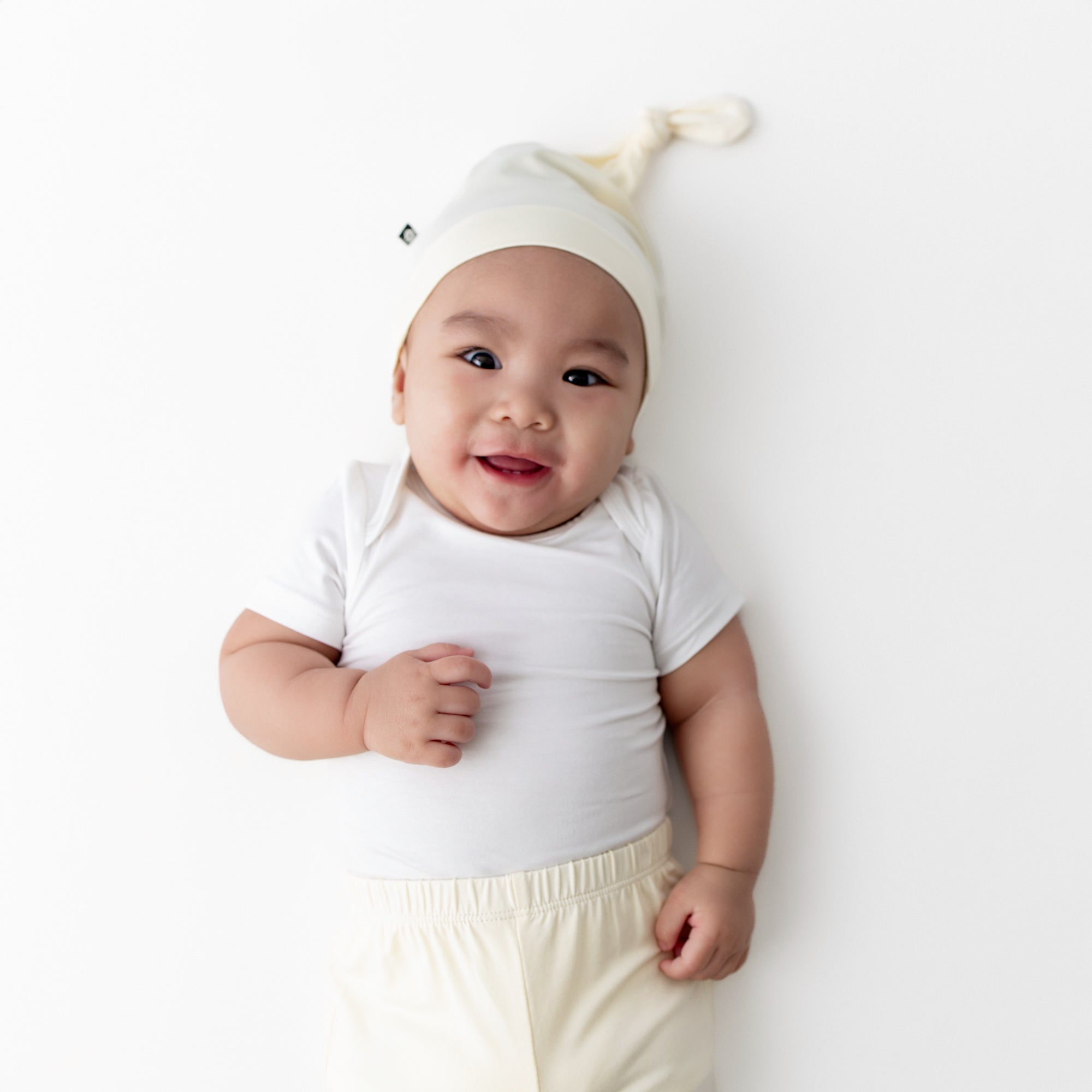 Smiling infant wearing the Knotted Cap in Chamomile with matching pants and white short sleeve bodysuit