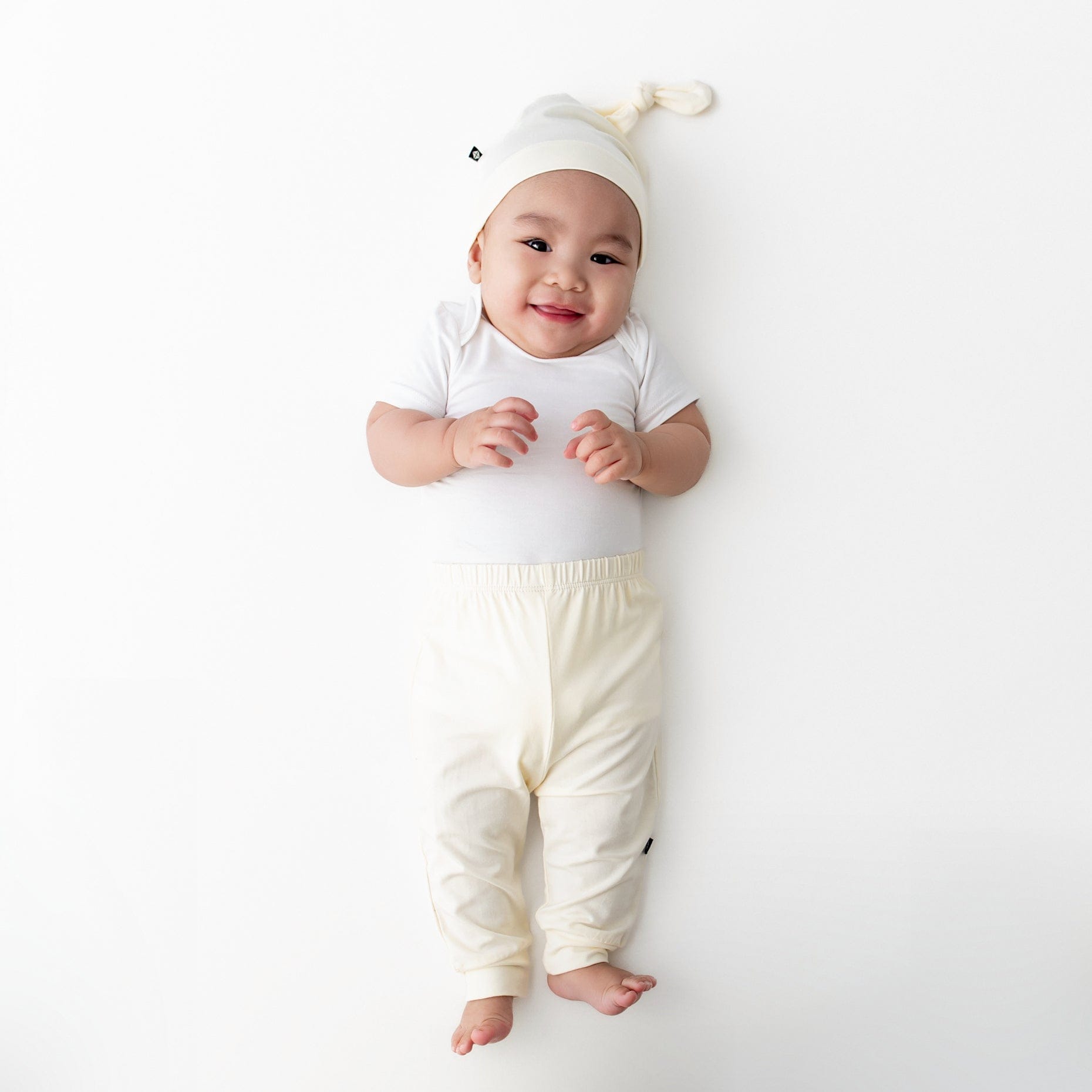 Infant laying on a light neutral surface wearing the Pant in Chamomile paired with matching knotted cap with white short sleeve bodysuit