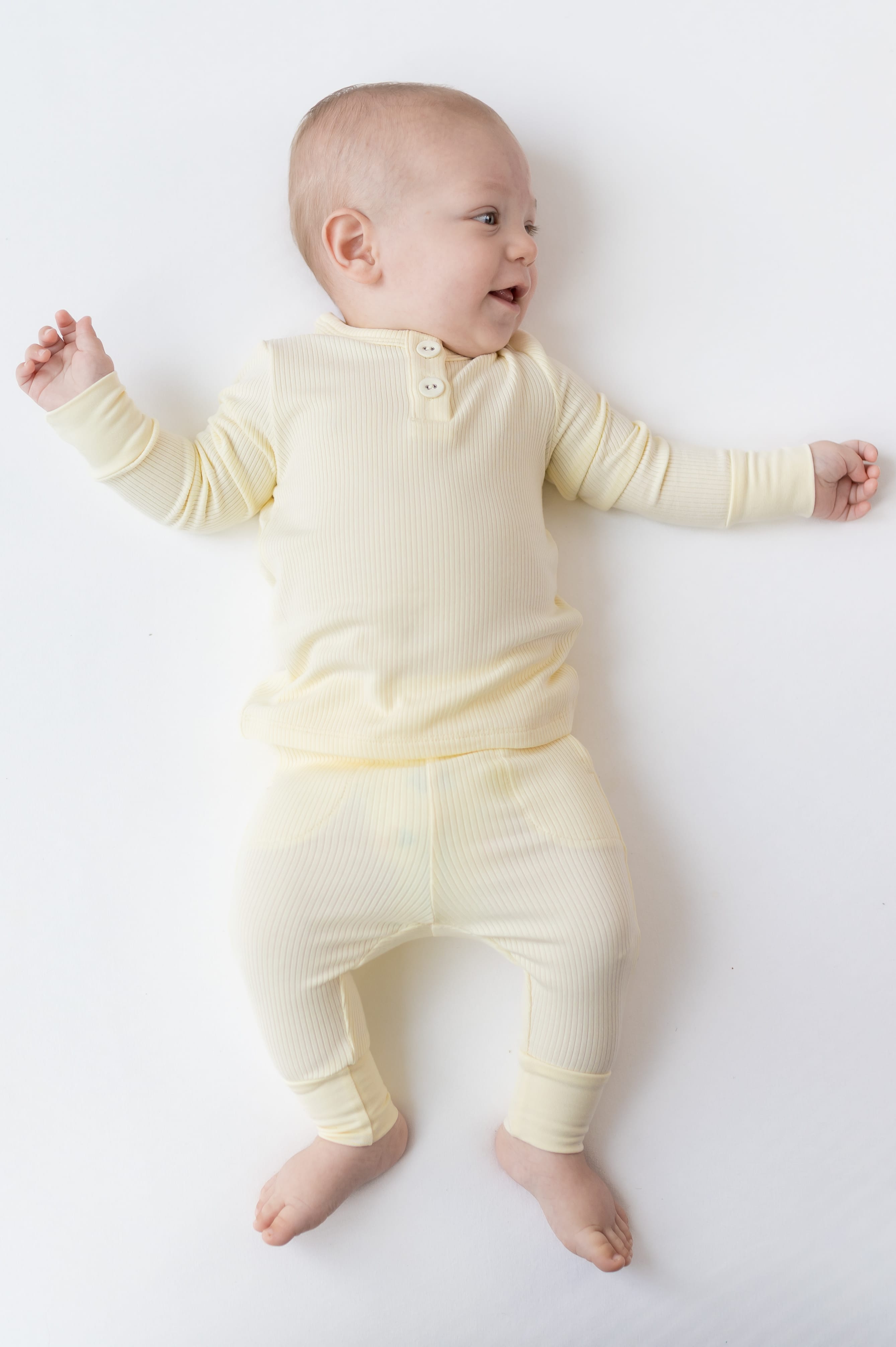 Smiling infant laying on a white surface wearing the Ribbed Infant Henley Set in Chamomile