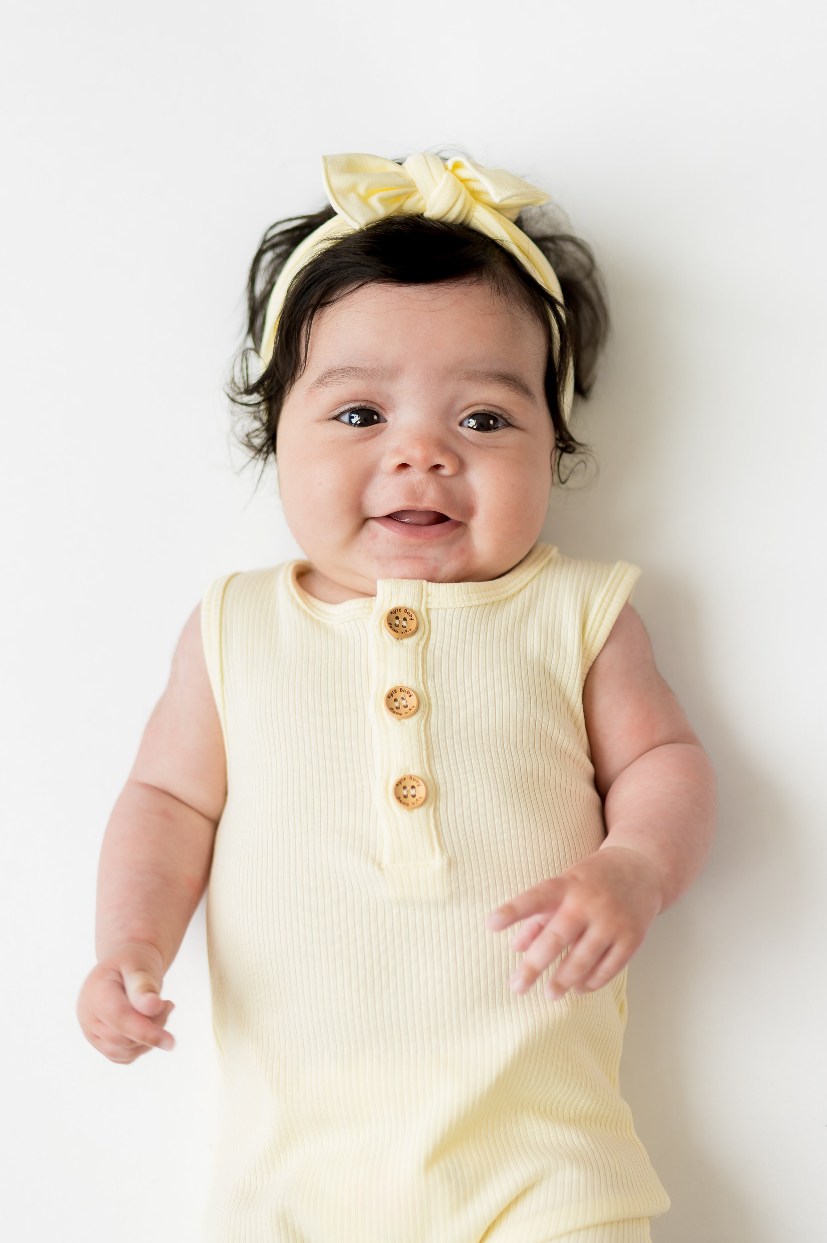 Close up of infant wearing the Ribbed Sleeveless Shortall in Chamomile showing the kyte baby engraved wooden buttons