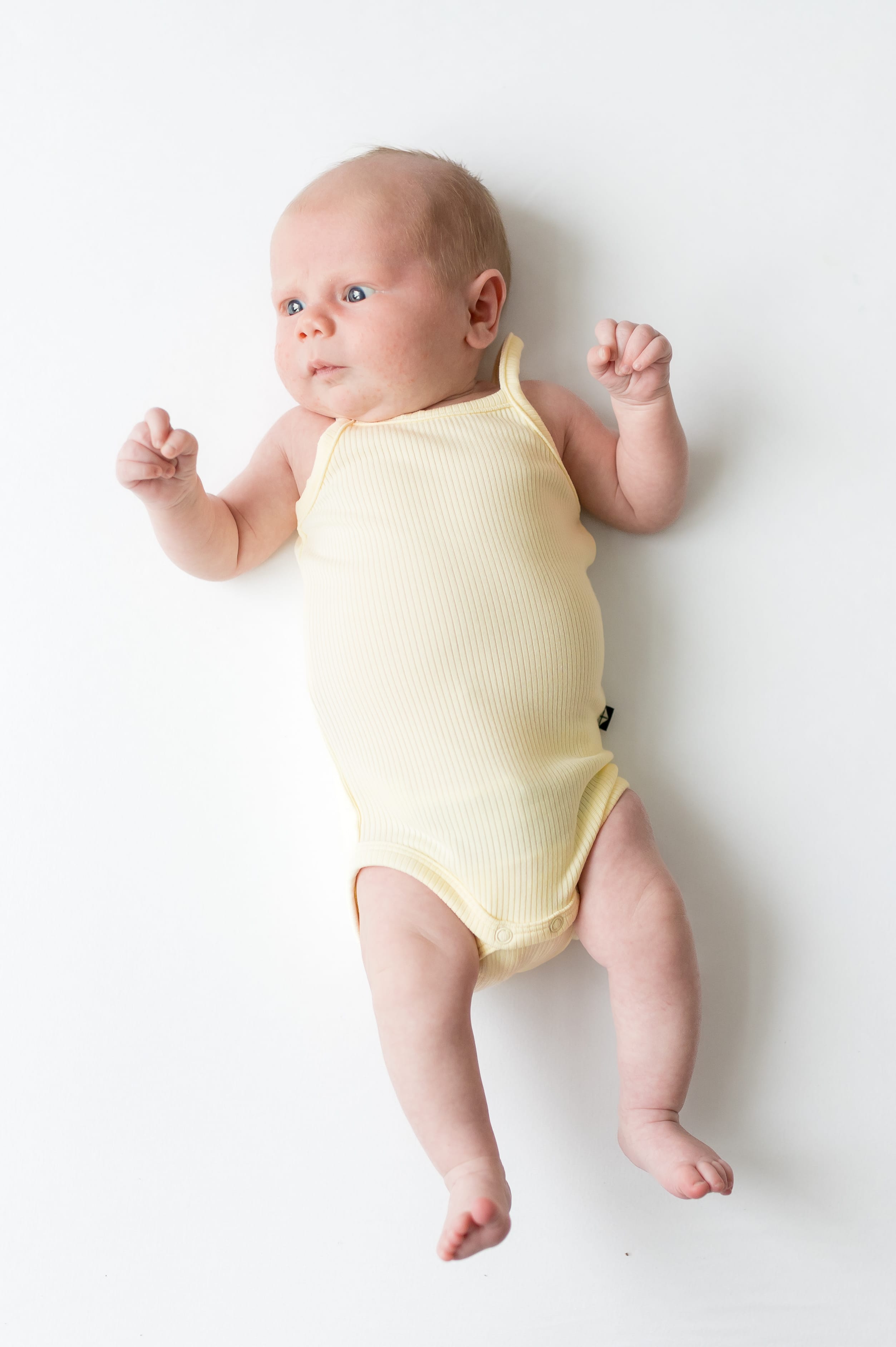 Newborn laying on a white surface wearing the Ribbed Spaghetti Strap Bodysuit in Chamomile