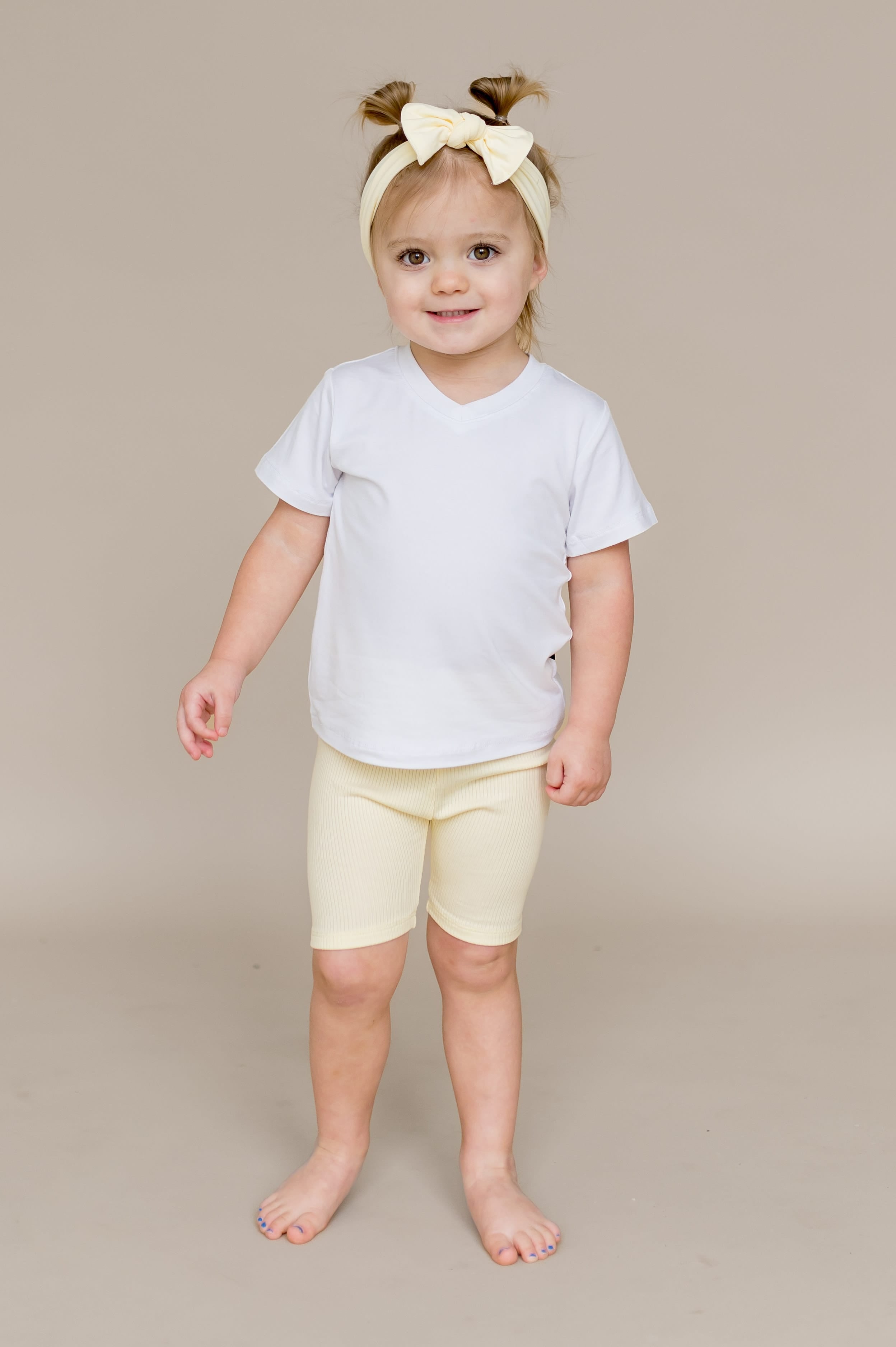 Young girl wearing the Ribbed Toddler Biker Shorts in Chamomile with a whitev-neck