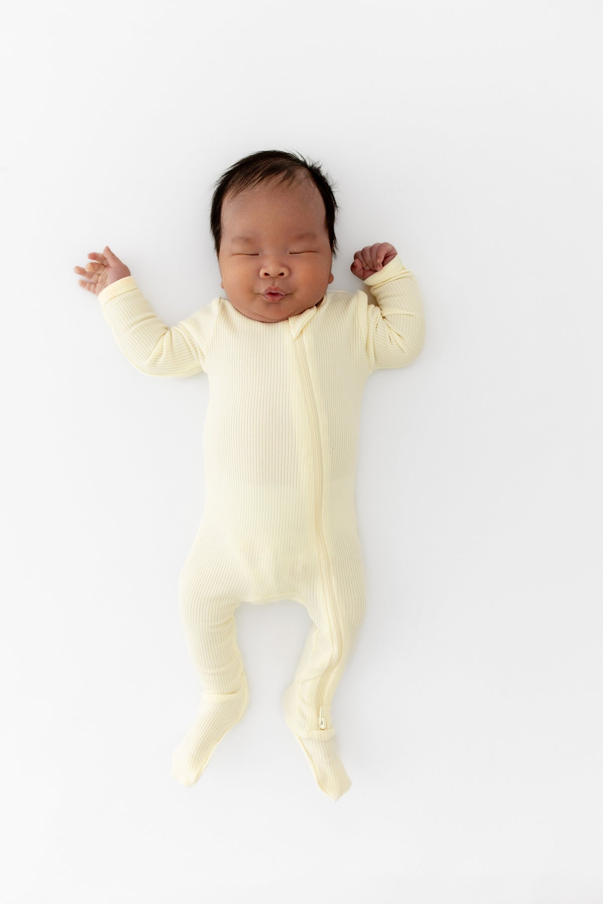 Newborn laying on a white surface wearing the Ribbed Zipper Footie in Chamomile