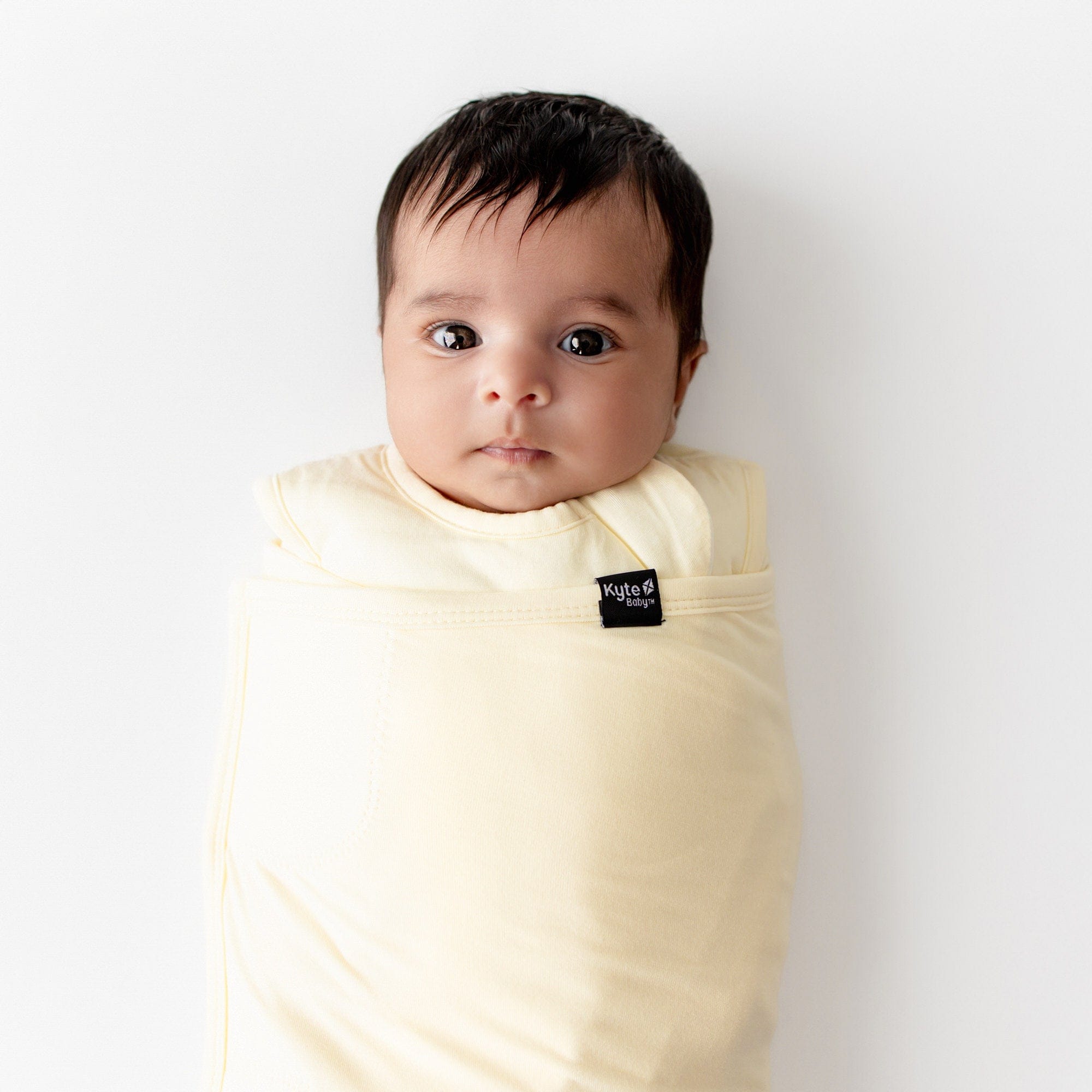 Baby wrapped in a yellow colored swaddle with a visible kyte baby label on a white background