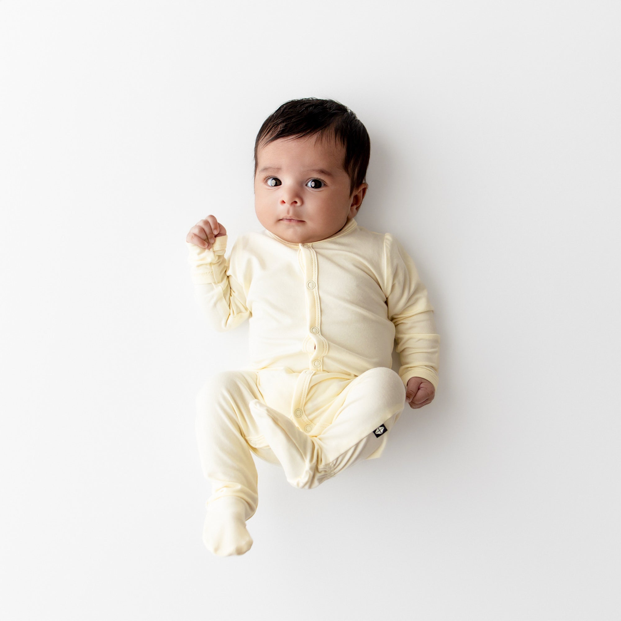Baby wearing a yellow colored footie with snap closures on a white background