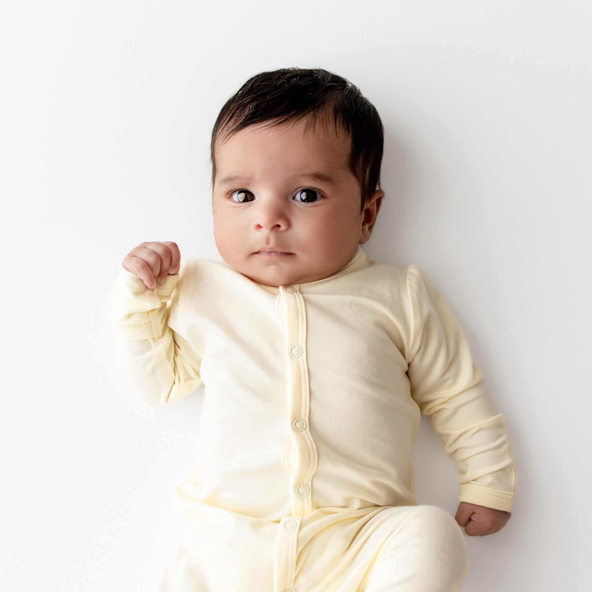 Baby wearing a yellow footie against a white background