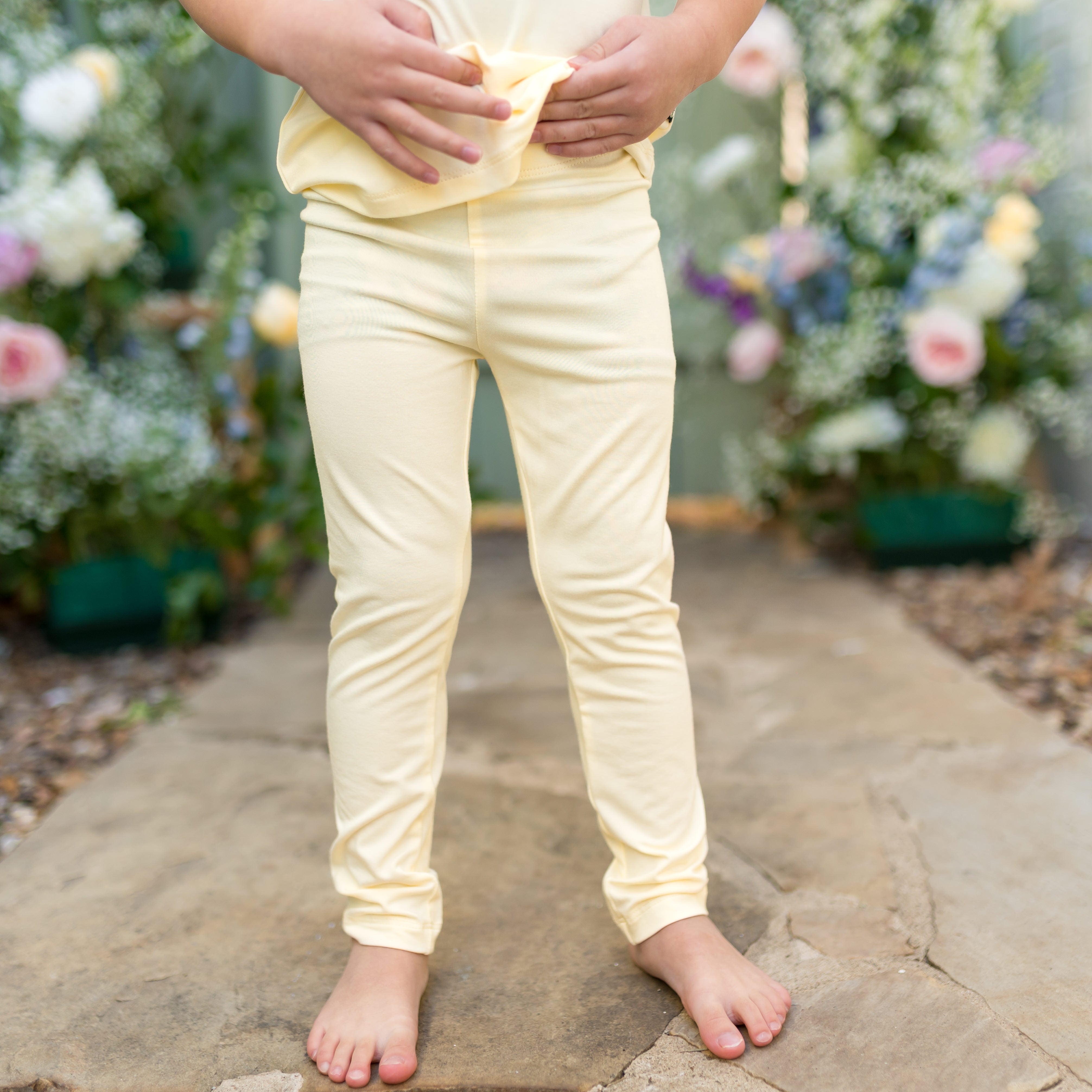 Child wearing light yellow leggings standing on a stone path with flowers in the background
