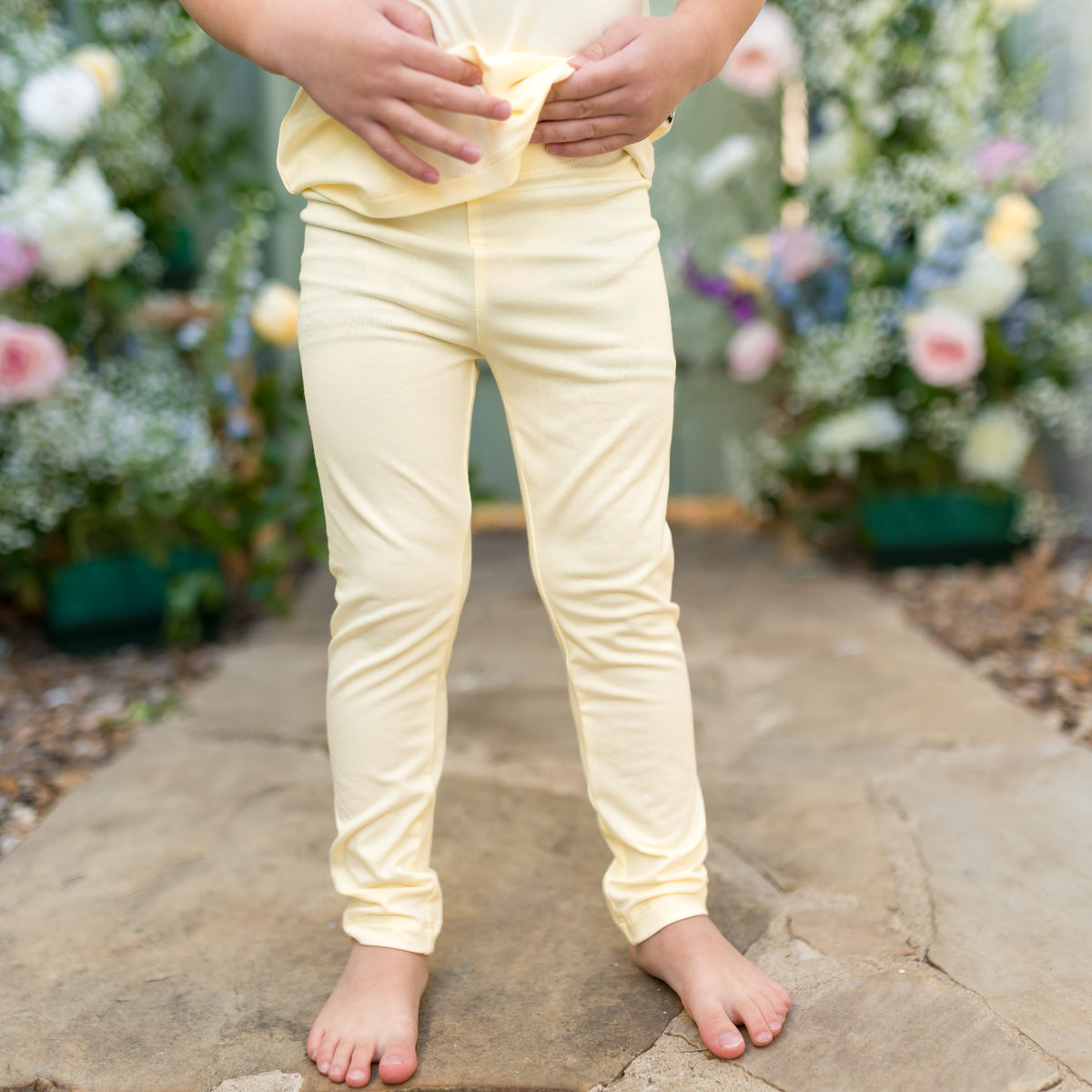 Child wearing light yellow leggings standing on a stone path with flowers in the background