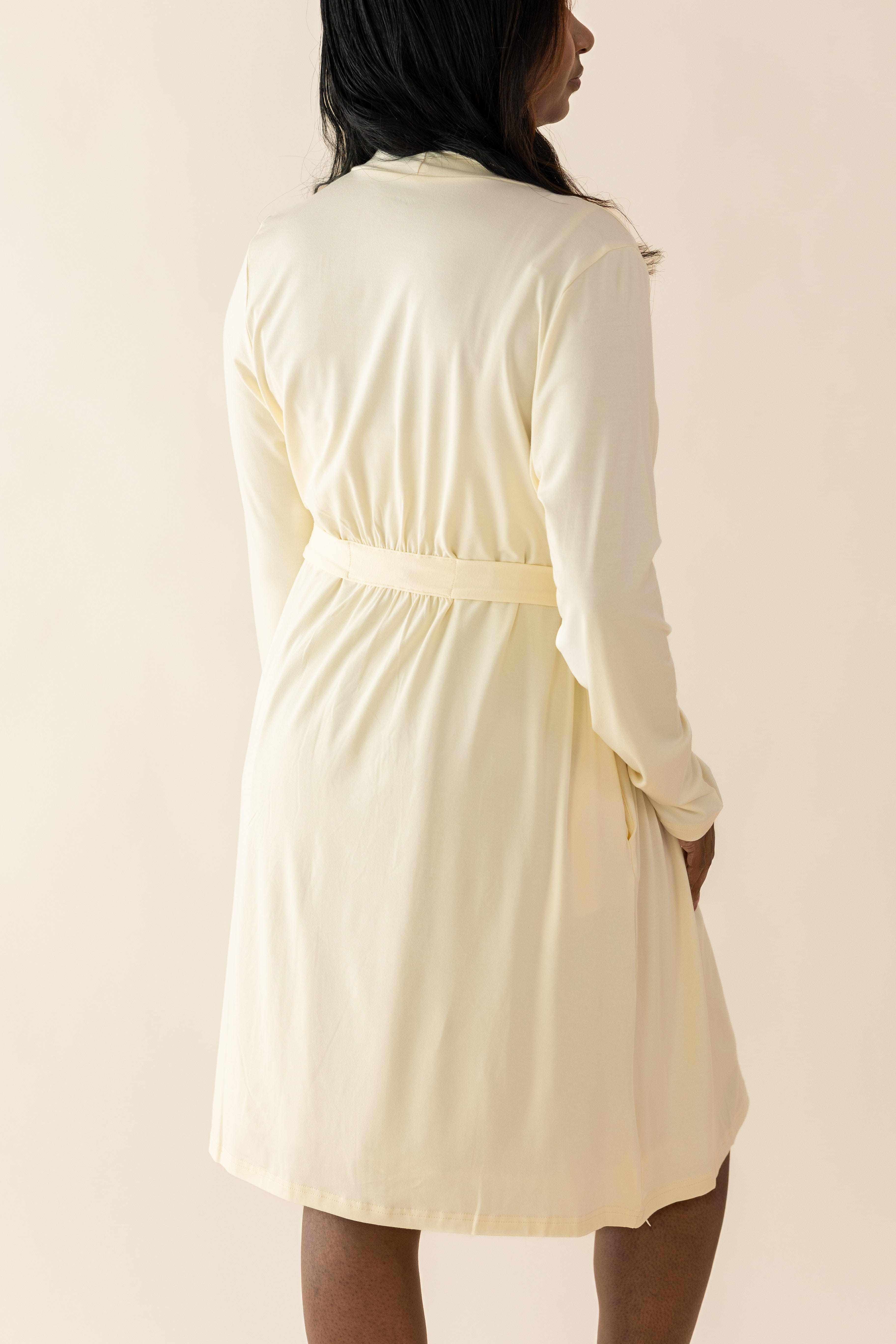 Woman wearing a yellow-colored lounge robe with long sleeves on a plain background