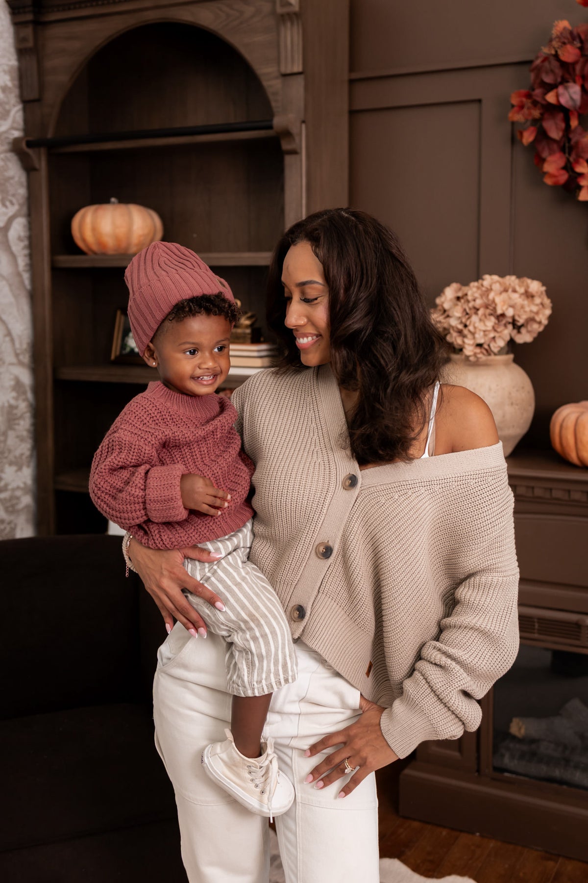 Modal wearing Chunky Knit Women's Cropped Cardigan in Almond holding toddler wearing chunky knit ribbed beanie and Chunky knit sweater in ember