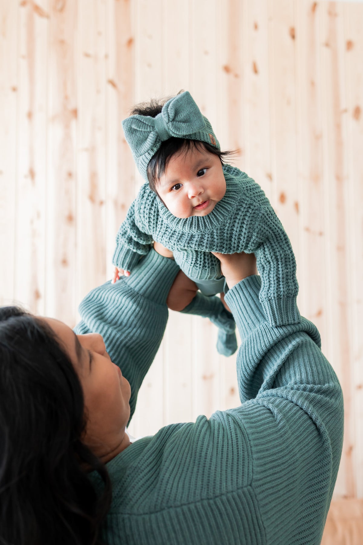Baby wearing Chunky Knit Sweater and chunky knit bow headband in pine held by mommy