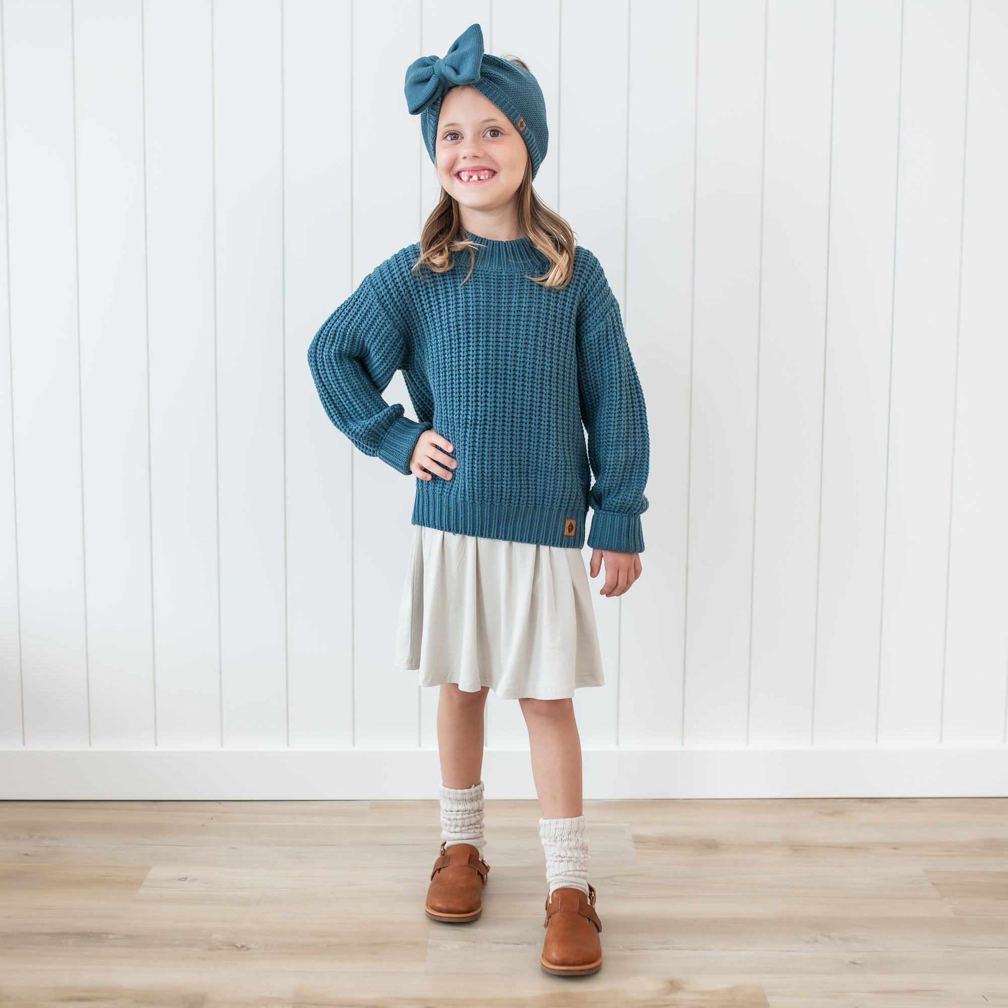 Girl model standing with one hand on hip wearing the Chunky Knit Sweater in Atlantic and matching chunky knit bow headband