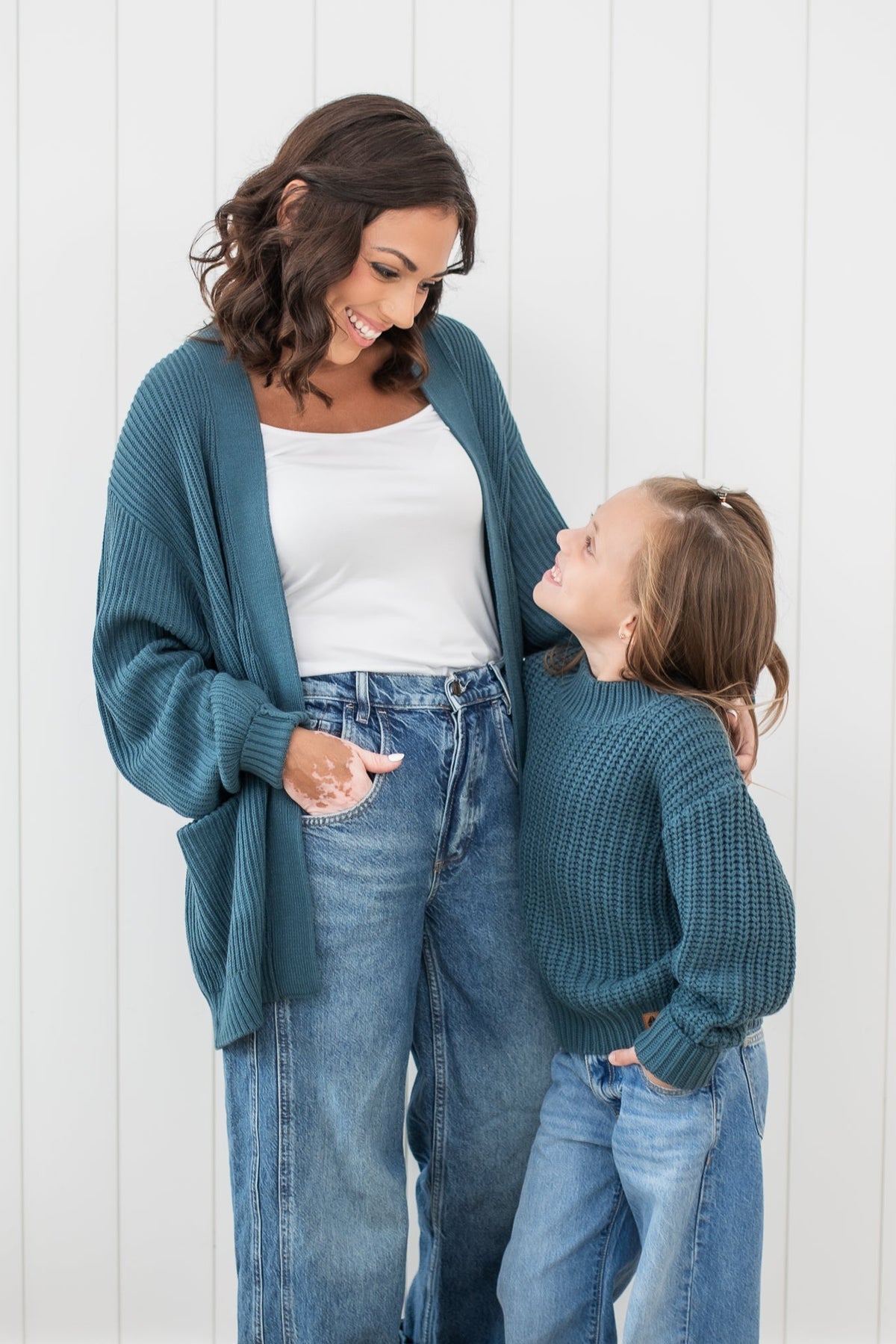 Mother and daughter standing looking at one another wearing the Chunky Knit Women's Oversized Cardigan in Atlantic and Chunky knit sweater in atlantic
