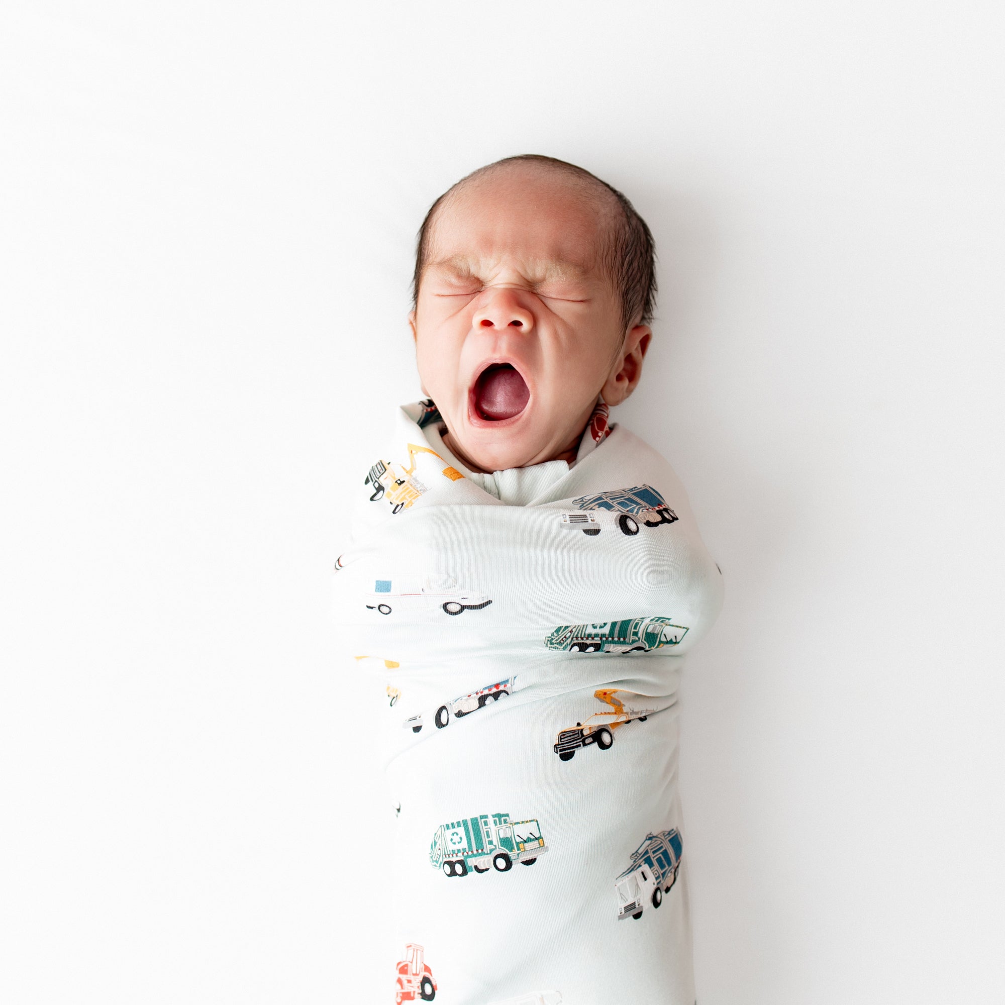 Close up of newborn yawning swaddled in the Swaddle Blanket in City Vehicles