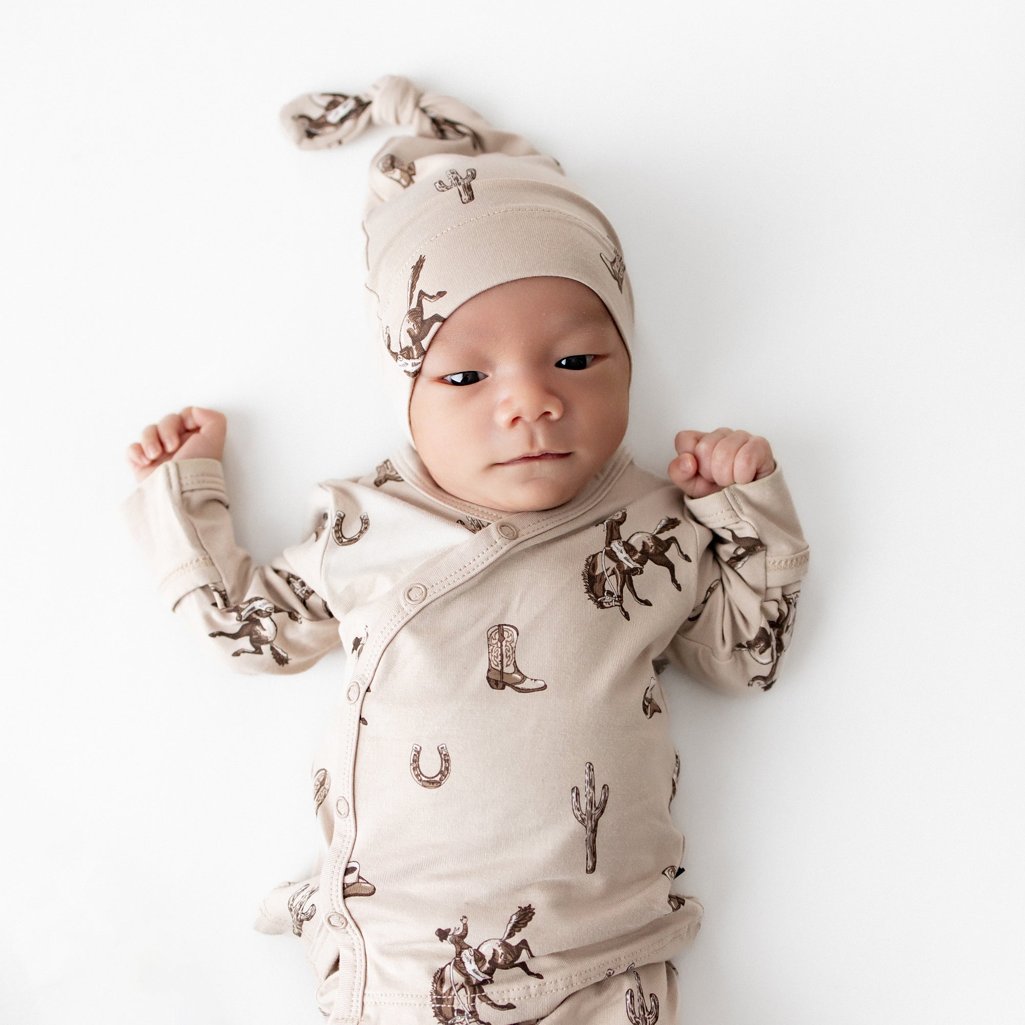 Close up of an newborn wearing the soft Take Me Home Set with Cap in Classic Cowboy from Kyte Baby laying on a cream surface