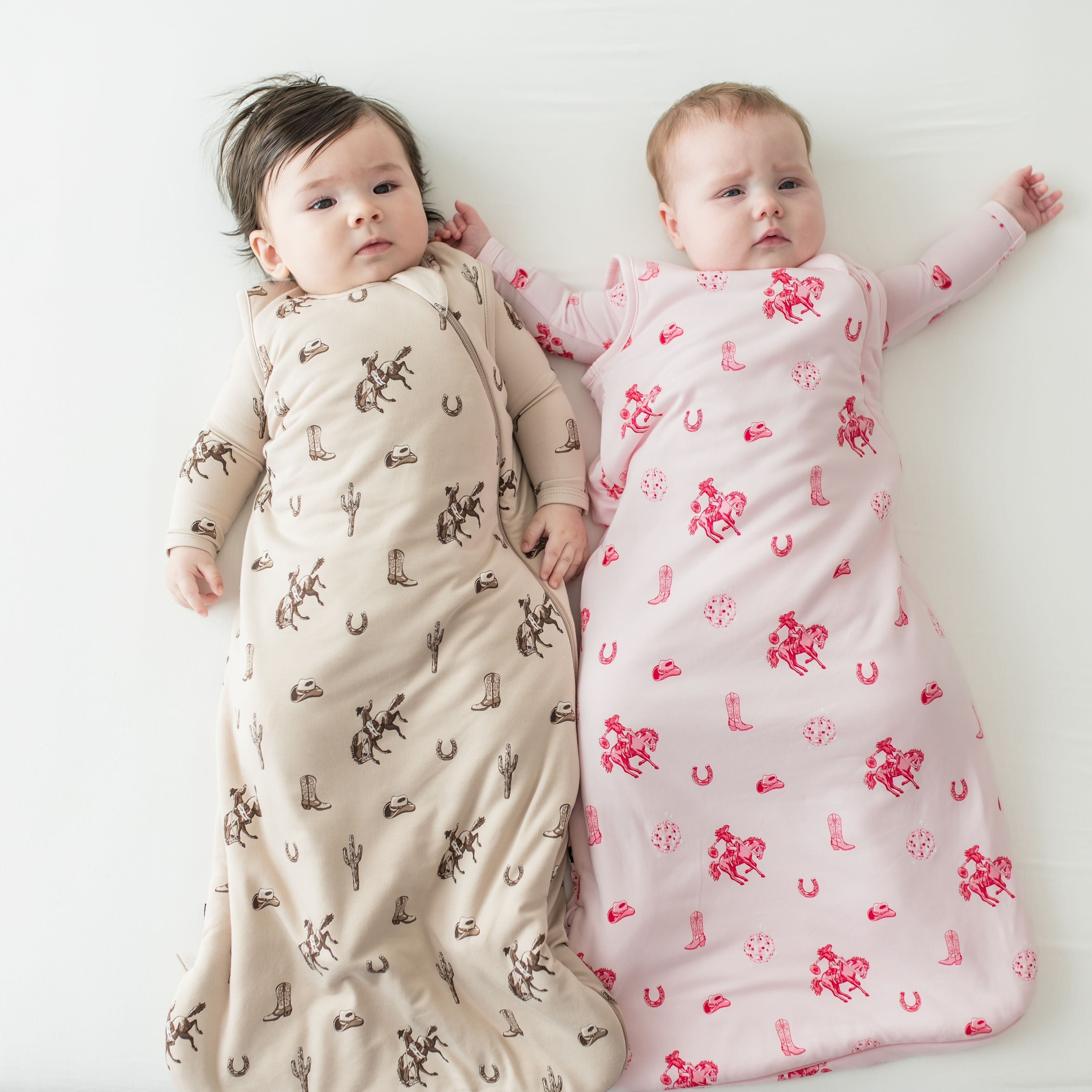 Two infants laying side by side wearing the classic cowboy and Disco Cowgirl 1.0 Sleep Bags
