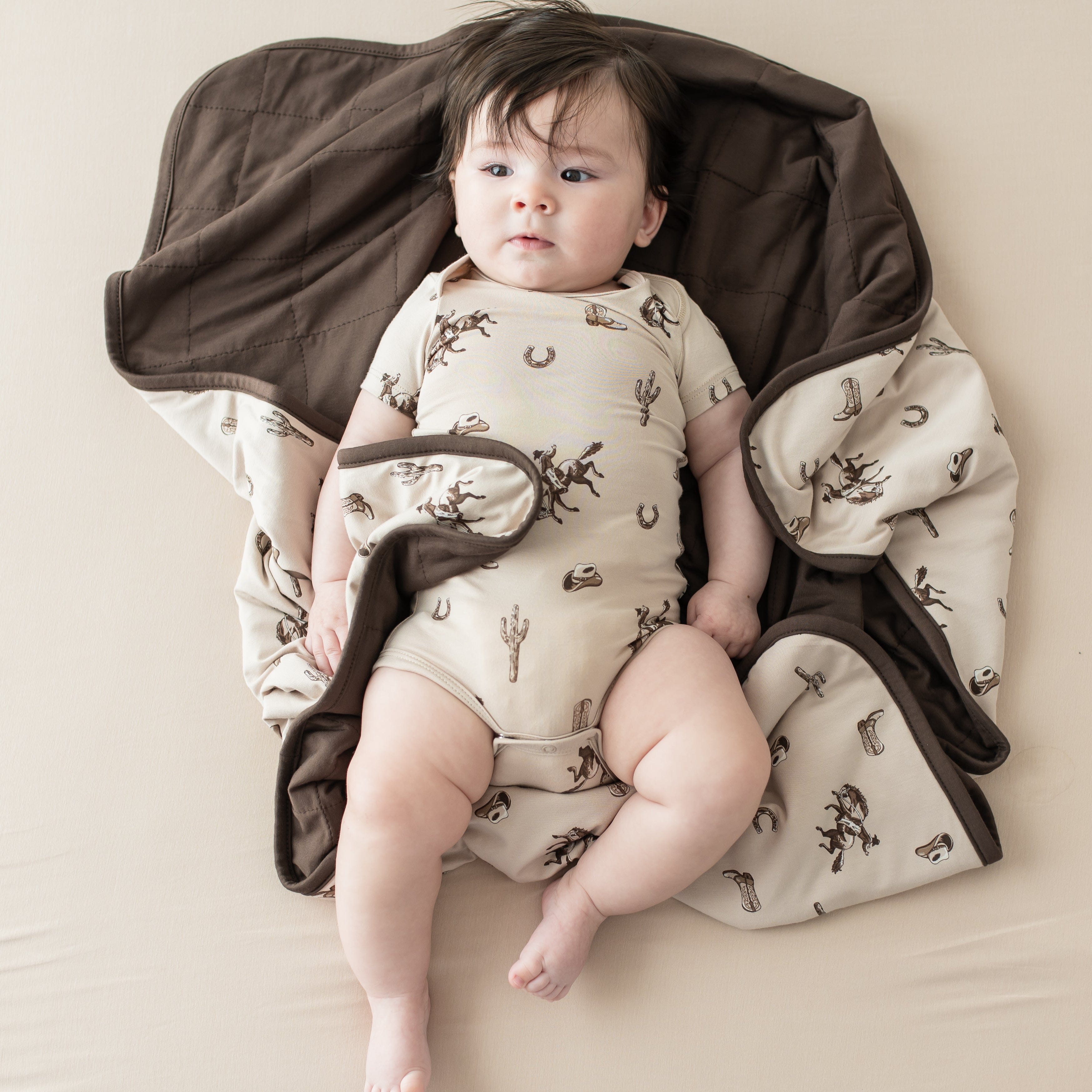 Infant wearing the Bodysuit in Classic Cowboy laying on a matching baby blanket