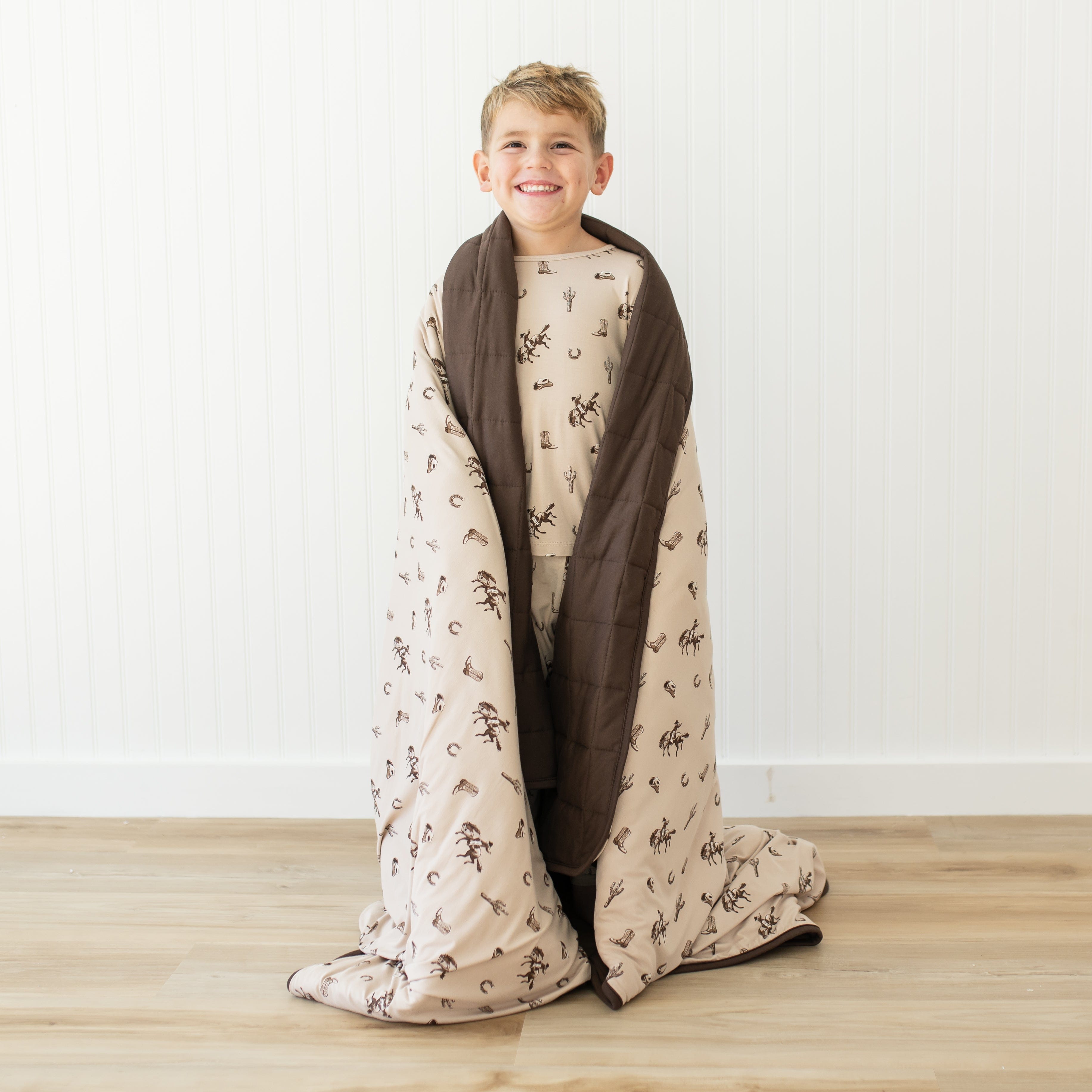 Young smiling boy standing with the Youth Blanket in Classic Cowboy 2.5 around his shoulders in front of a white paneled wall