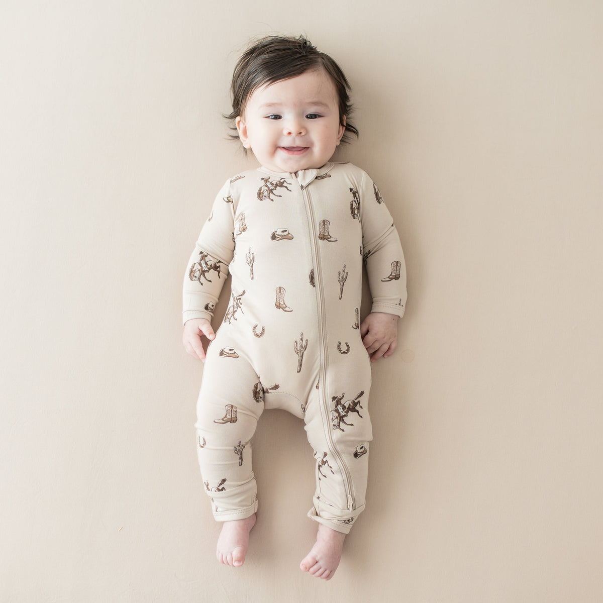 Infant laying on a light neutral surface wearing the Zippered Romper in Classic Cowboy