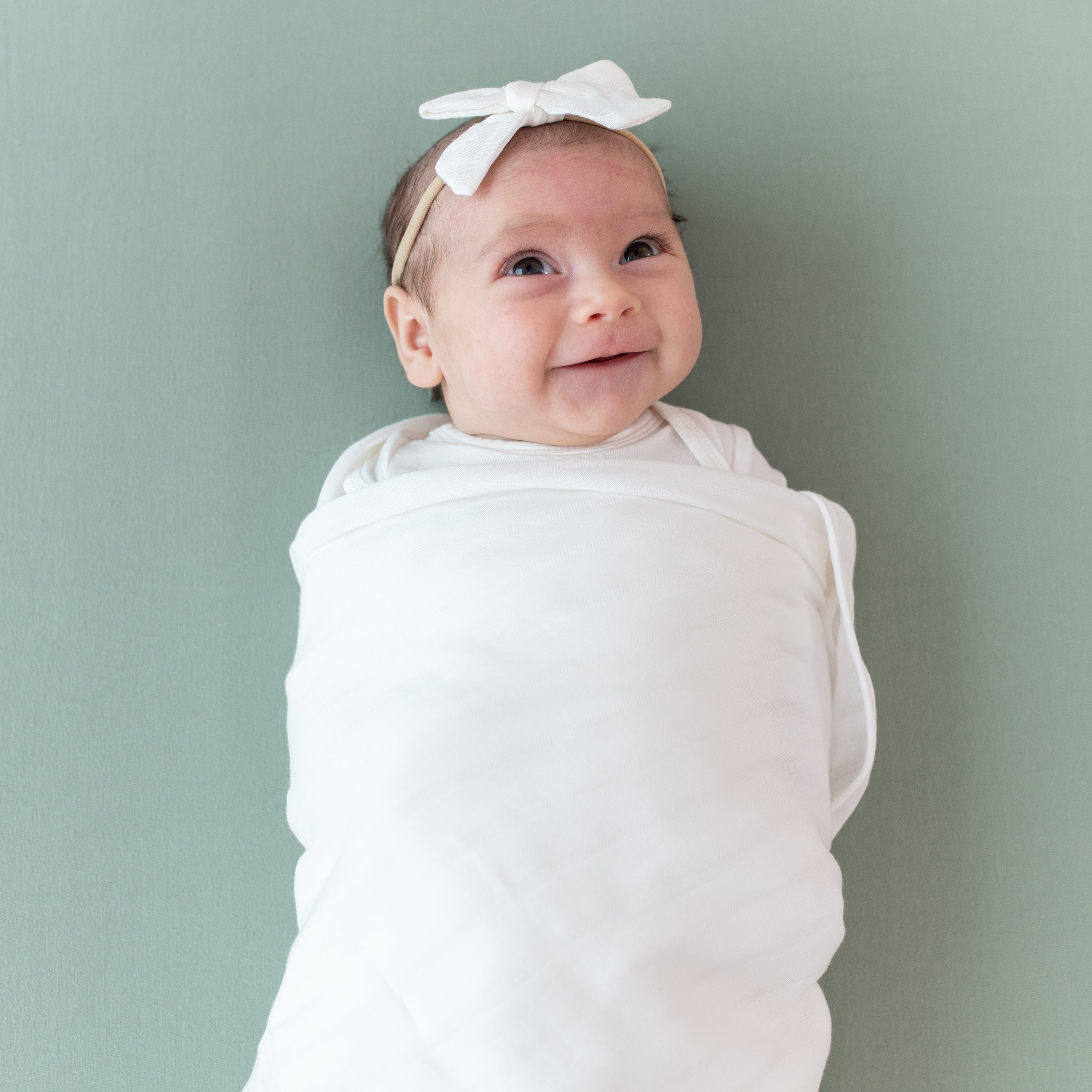 Baby wearing White Bamboo Muslin Swaddle Blanket in Cloud with Matching Bow