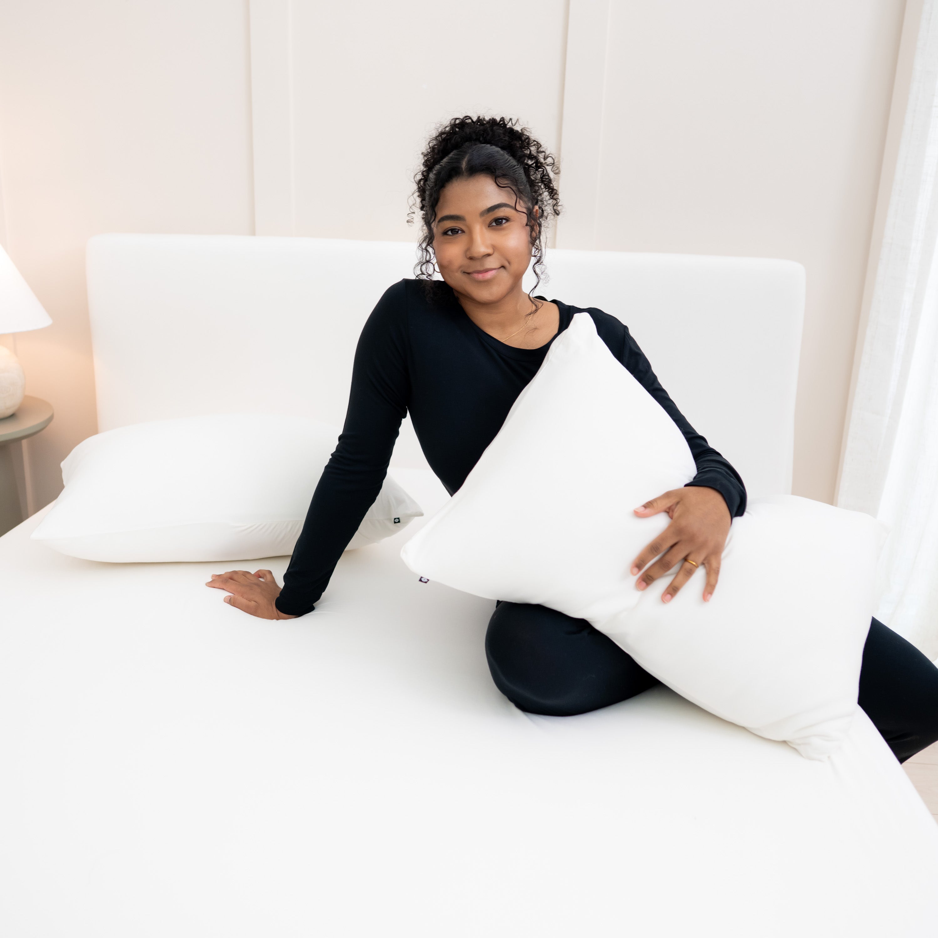 Woman on bed with Kyte Baby Fitted Sheet with Pillowcases in Cloud White