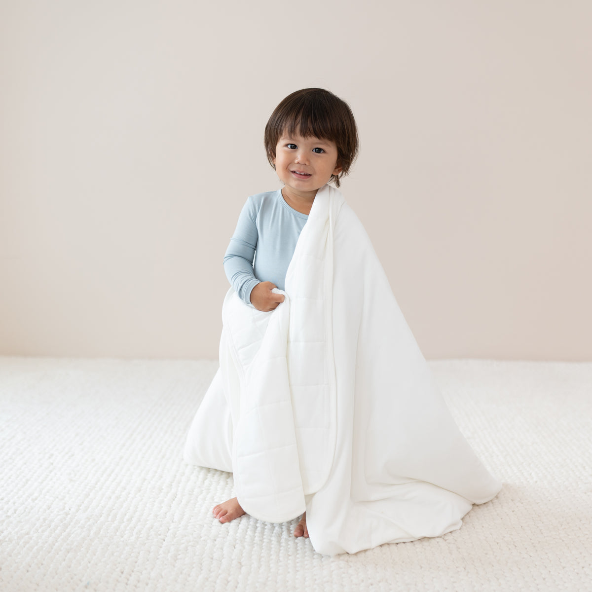 Toddler wrapped in a Toddler Blanket in Cloud 1.0 TOG while wearing a Long Sleeve Pajama Set in Fog