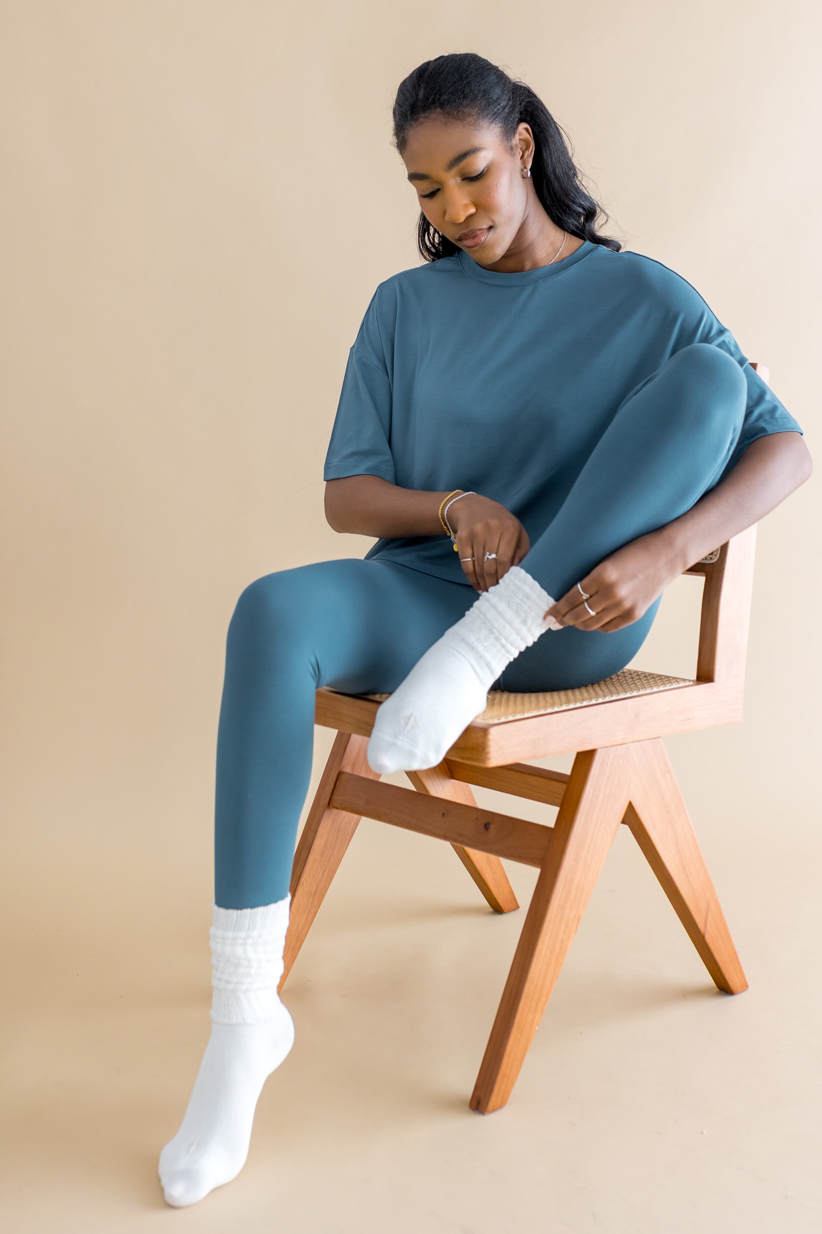 Model sitting on a wooden chair wearing the Adult Scrunch Socks in Cloud with blue leggings and a blue shirt
