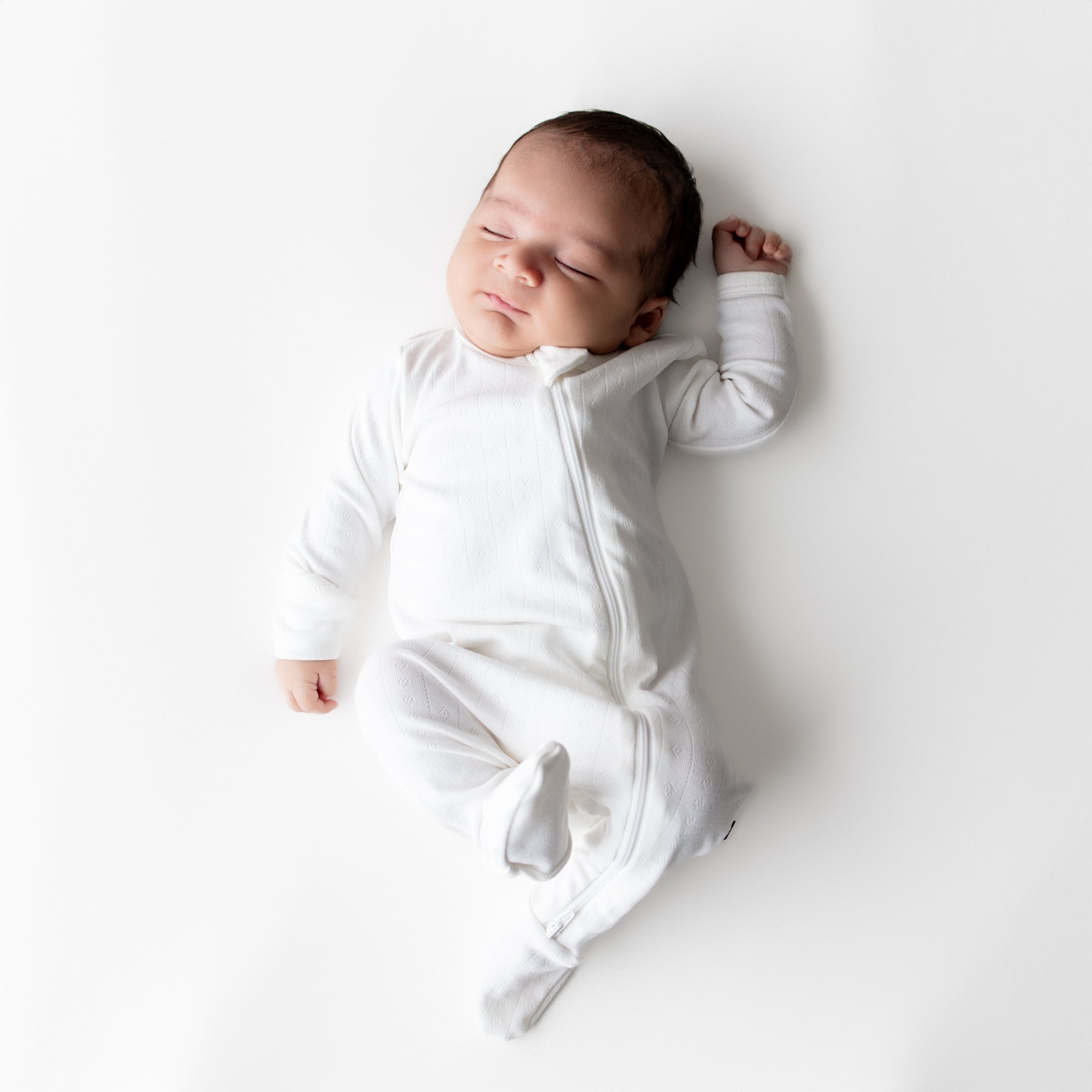 Sleeping newborn posing wearing the Pointelle Zippered Footie in Cloud