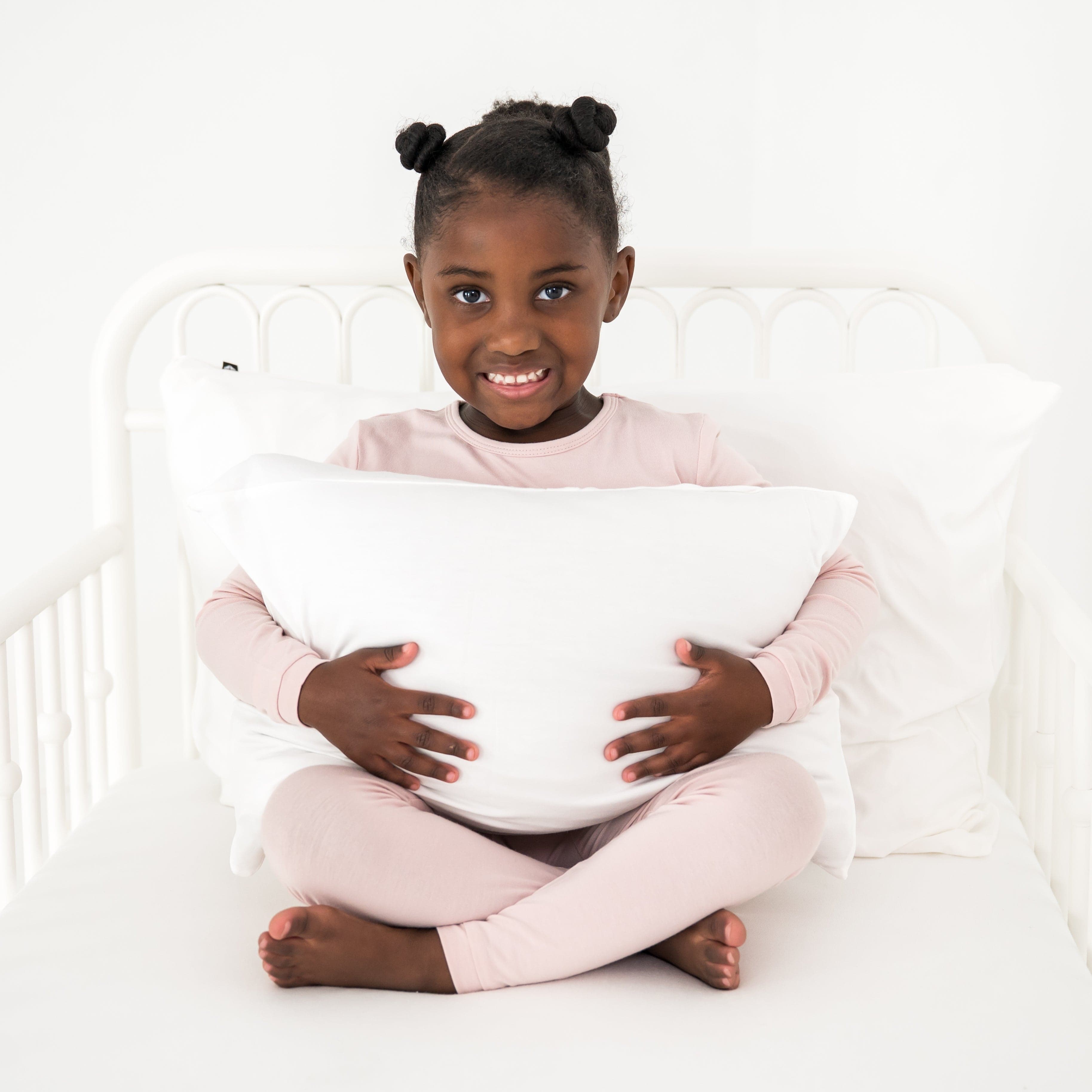 Young girl holding a soft white pillow in a white toddler bed