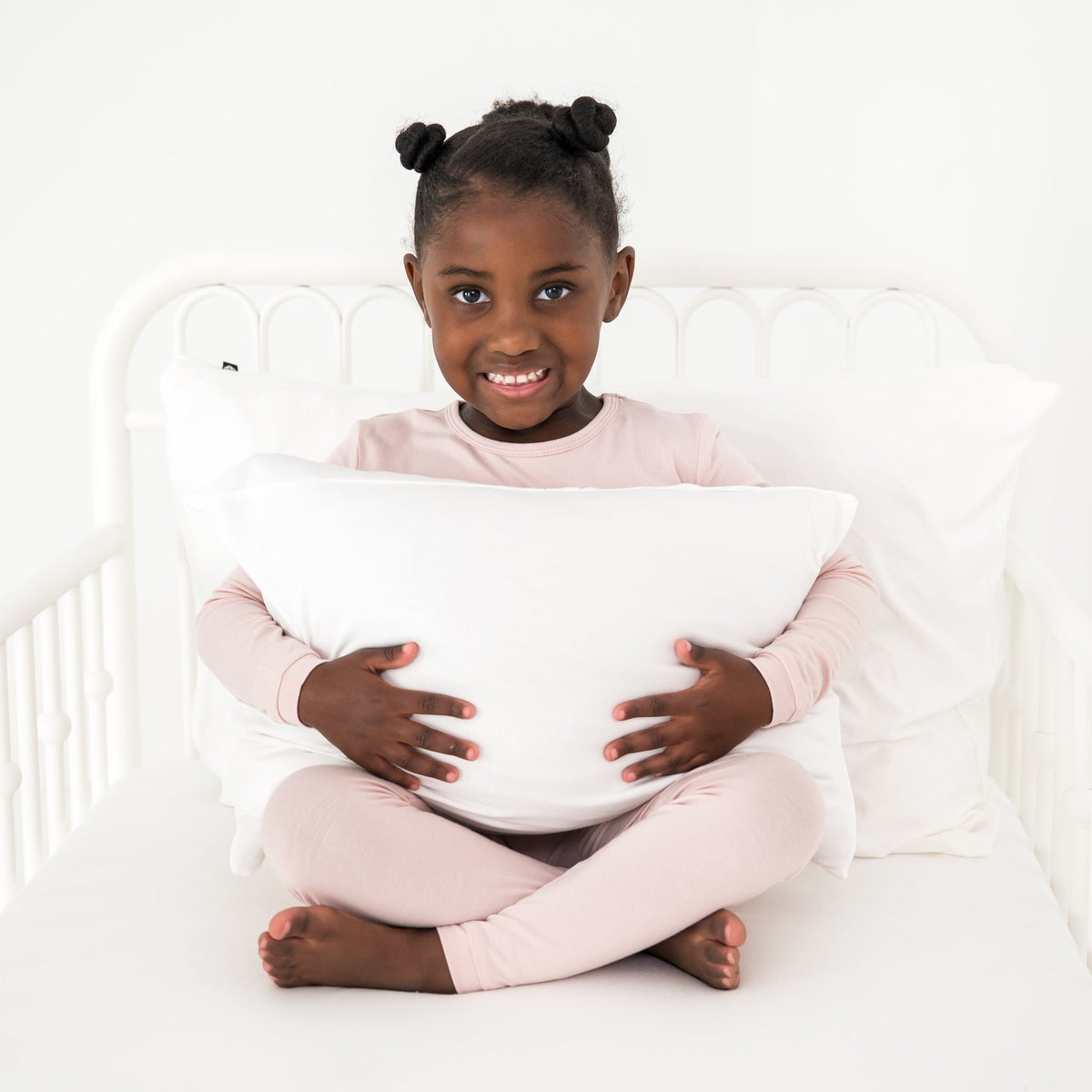 Young girl holding a soft white pillow in a white toddler bed