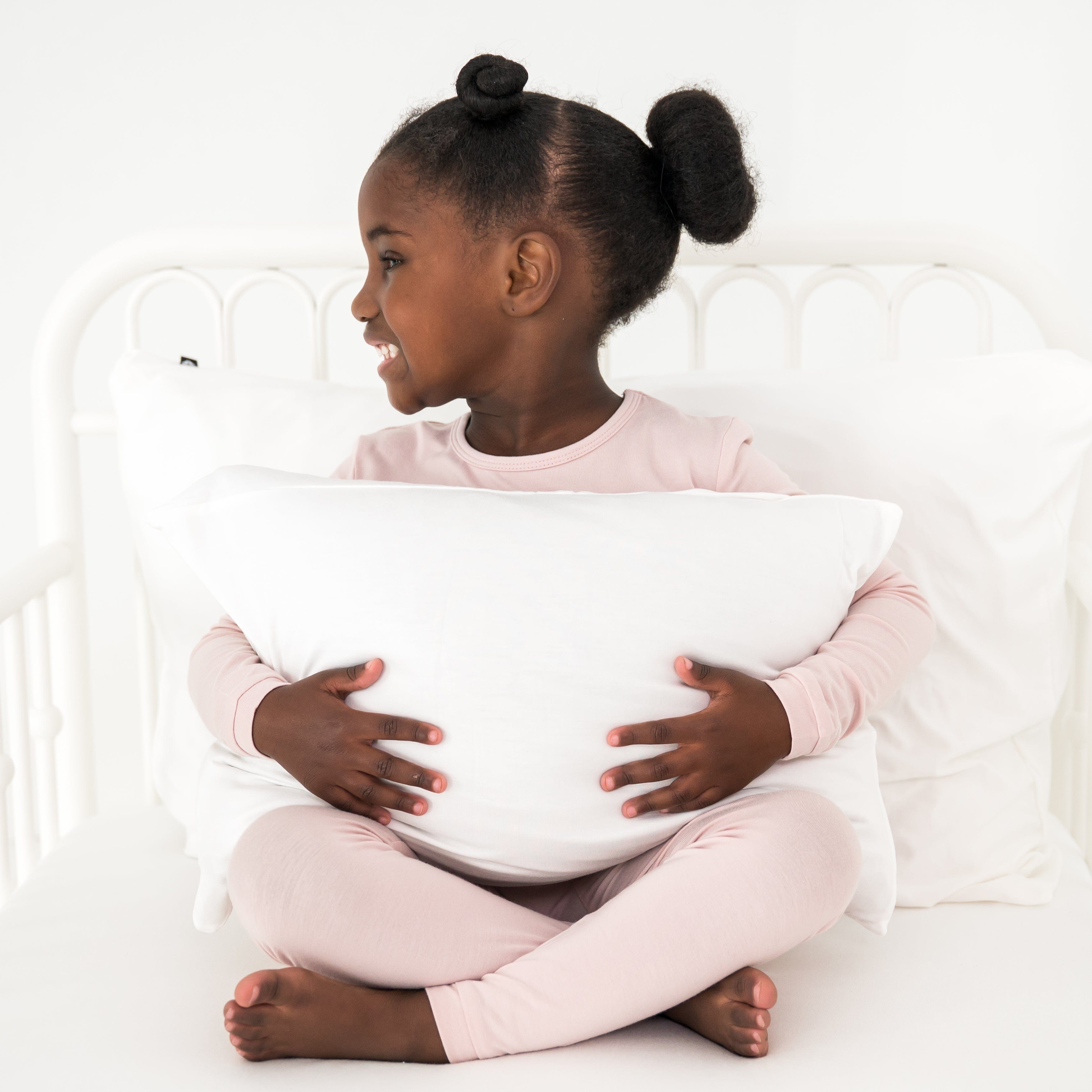 Young girl holding a pillow in a white bedroom
