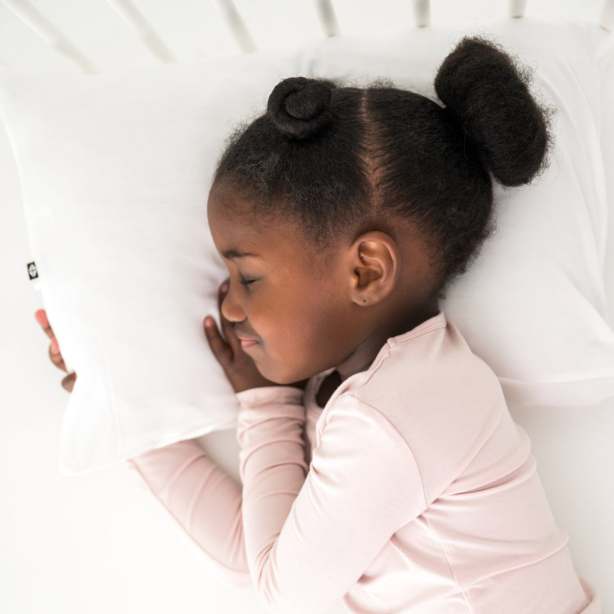 Child laying on white pillow wearing light pink pajamas