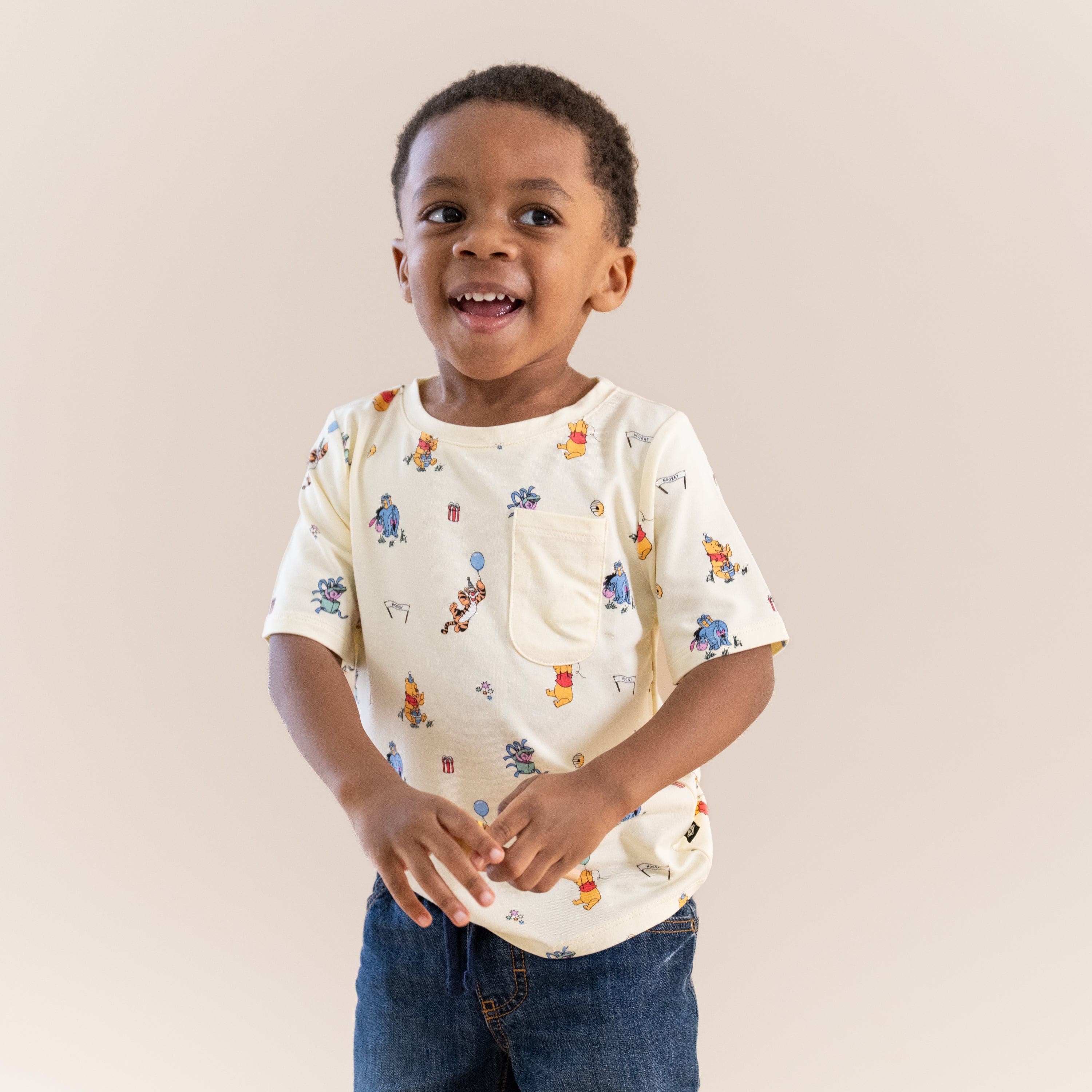 Young boy wearing the Toddler Crew Neck Tee in Winnie the Pooh Celebration paired with dark denim jeans
