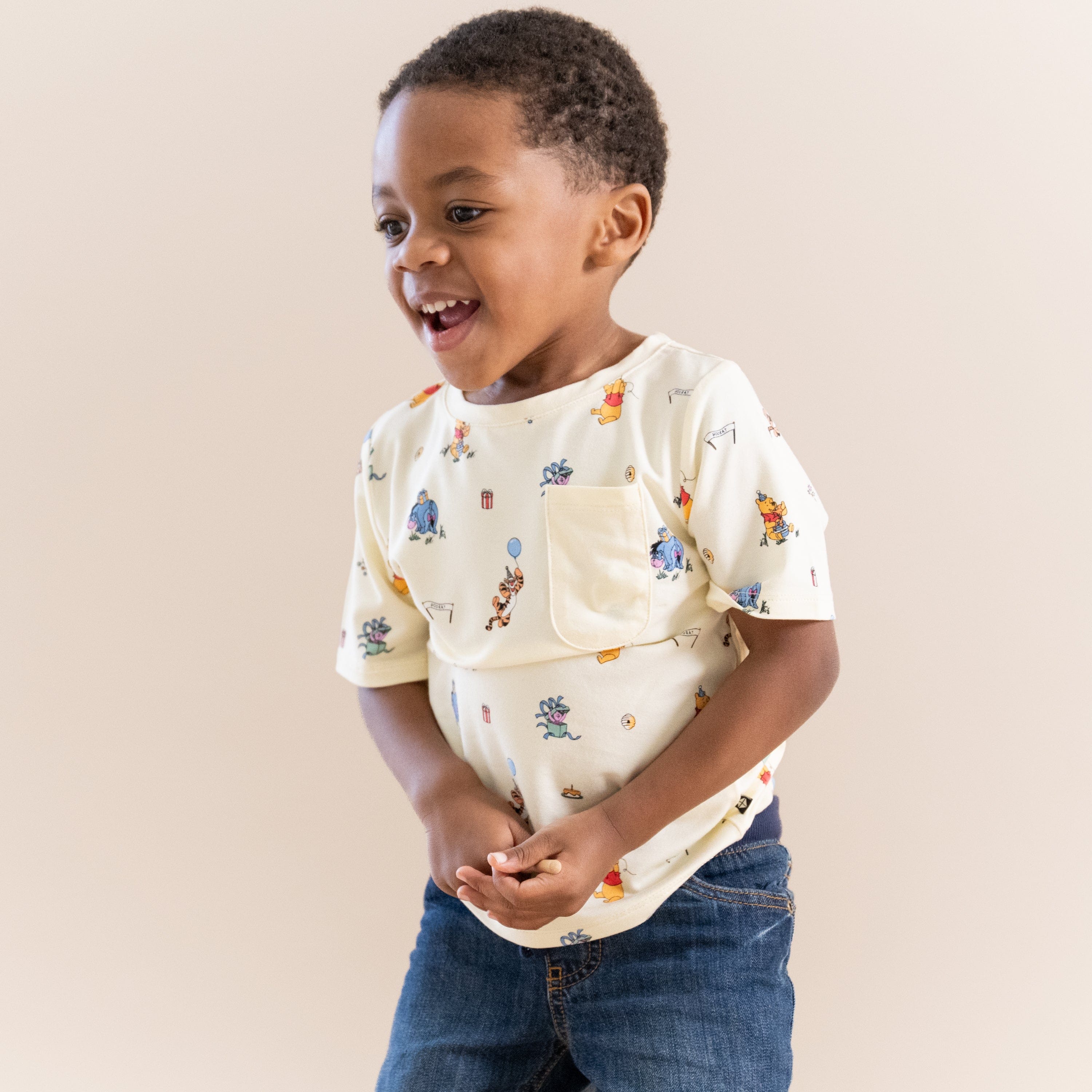 Smiling boy wearing the Toddler Crew Neck Tee in Winnie the Pooh Celebration with dark wash jeans