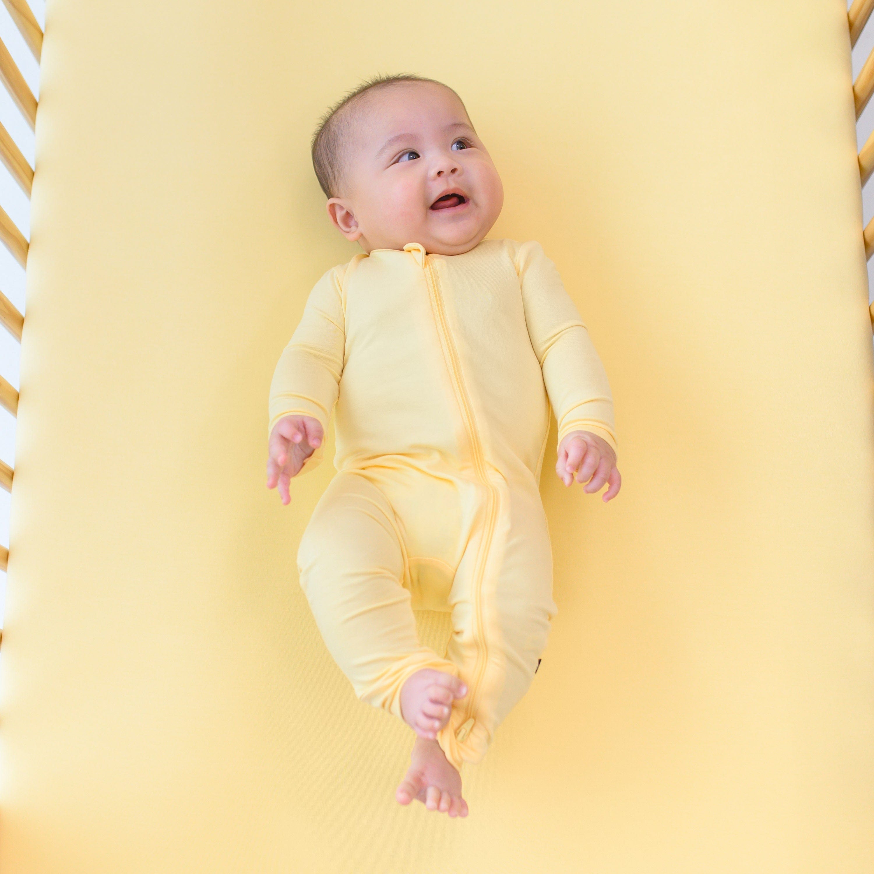baby wearing lilikoi zippered romper and laying on a crib with lilikoi crib sheet