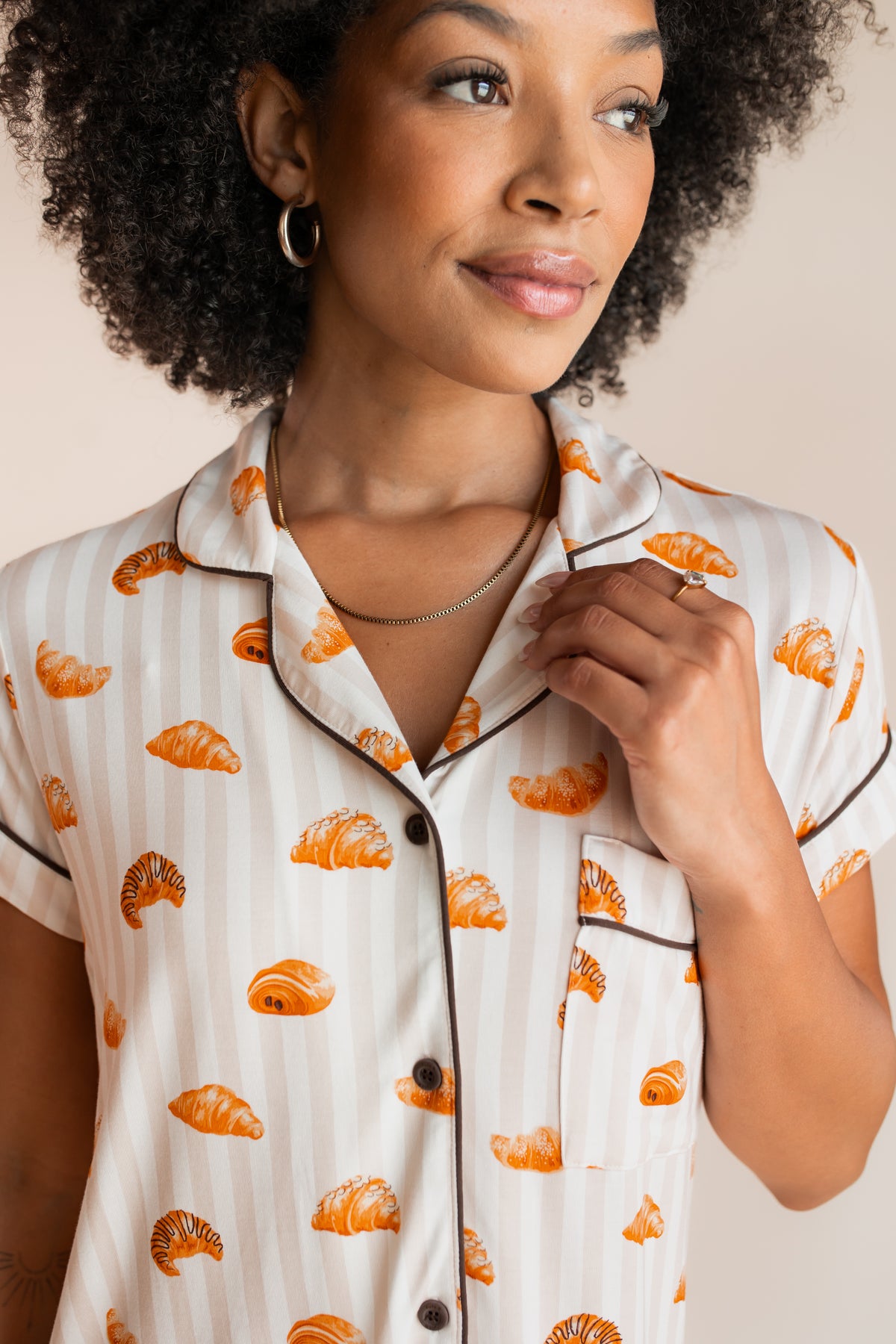 Model showcasing the shirt of Women's Short Sleeve Cropped Pajama Set with Croissant print with brown trim on a beige background