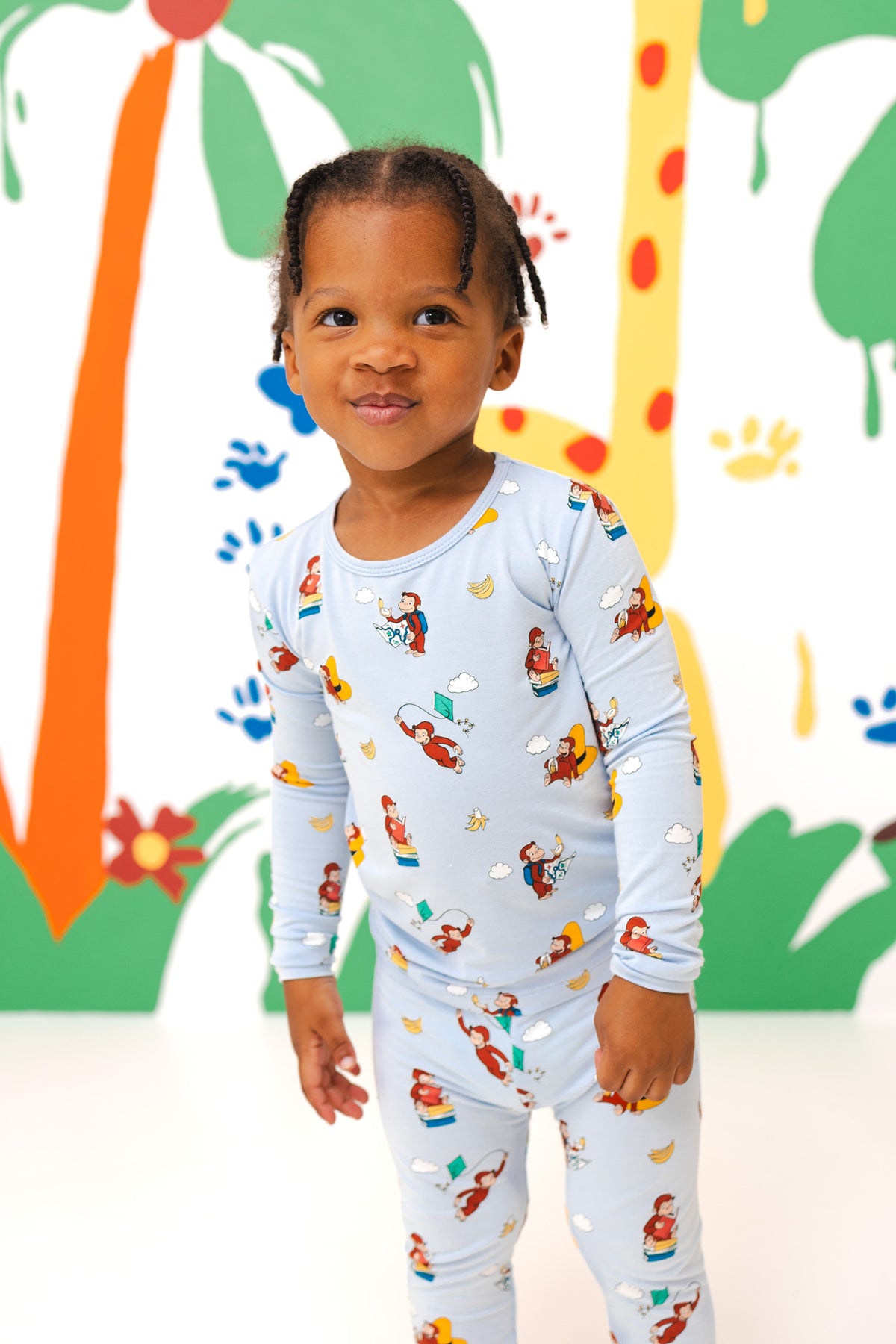Girl posing in Long Sleeve Pajamas in Curious George print standing in a colorful background