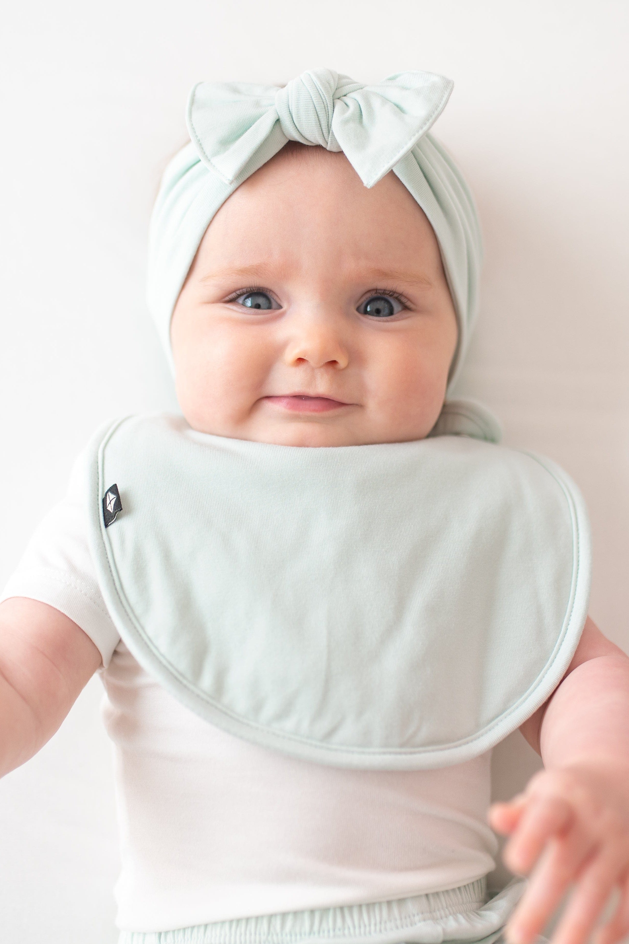 Infant model wearing the Cushy Bib in Dew paired with a matching knotted bow