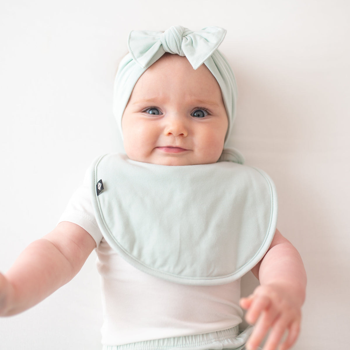 Infant model wearing the Cushy Bib in Dew paired with a matching knotted bow