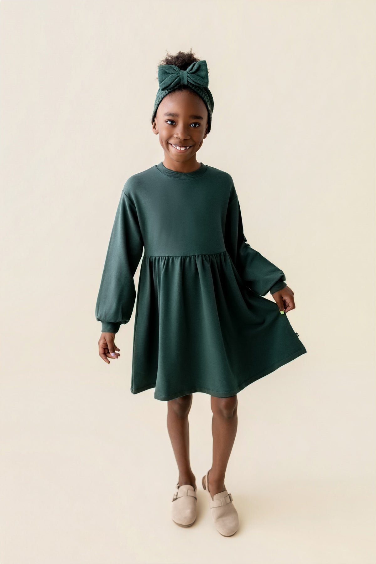 Girl wearing Long Sleeve Skater Dress in Cypress color on a beige background